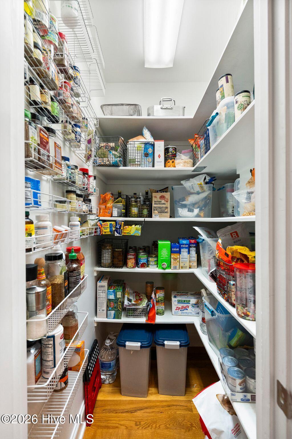 Walk-in pantry with densely stocked shelves and two large storage bins on the floor.
