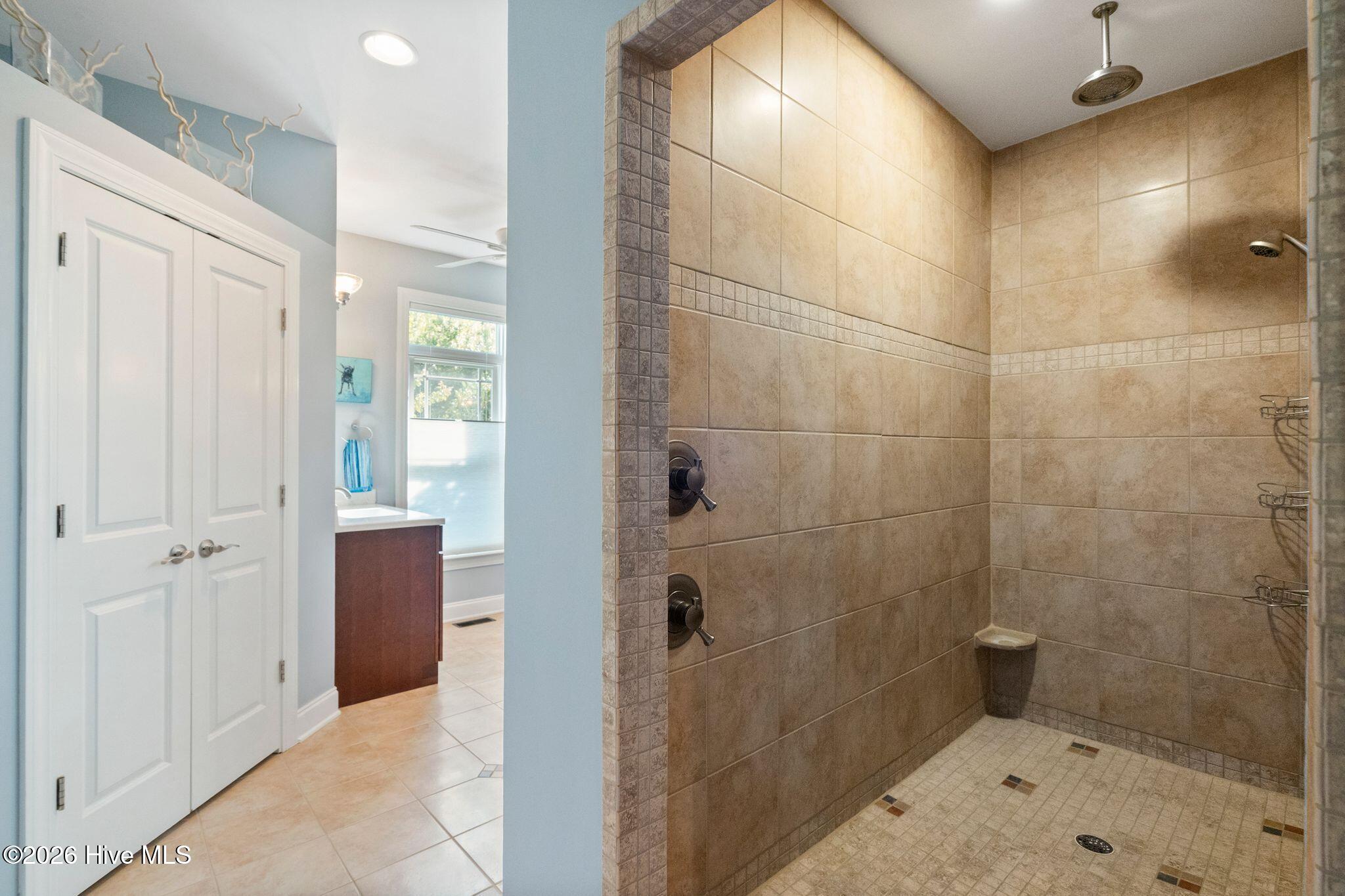 Walk-in shower with tan tile, a mosaic accent band, and dark bronze fixtures.