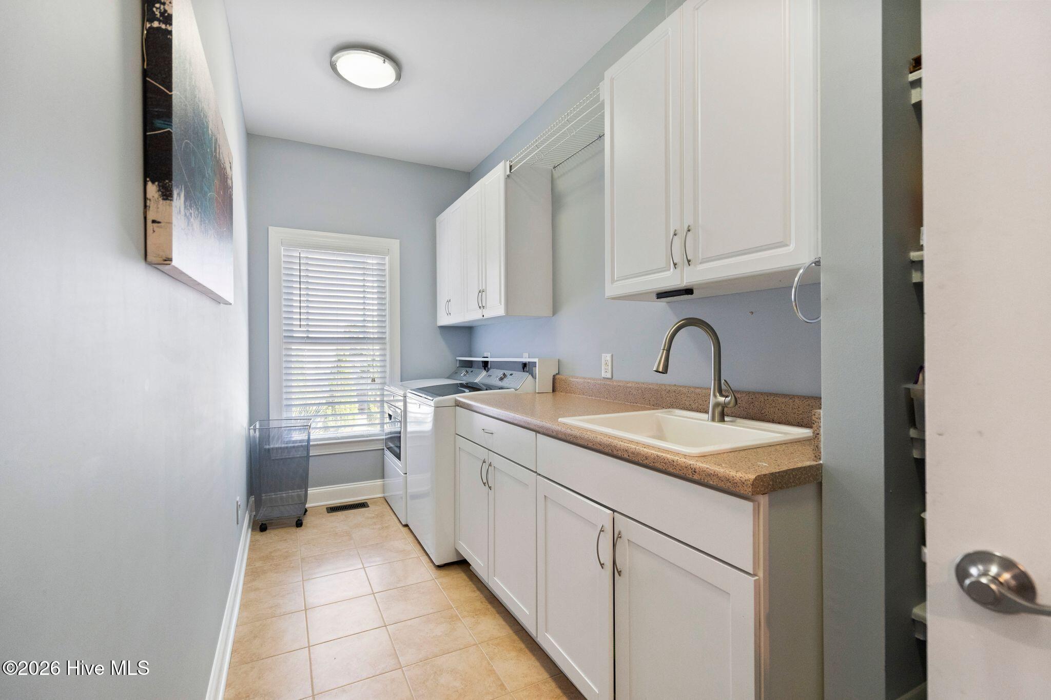 Laundry room with washer and dryer, white cabinets, and a countertop utility sink.