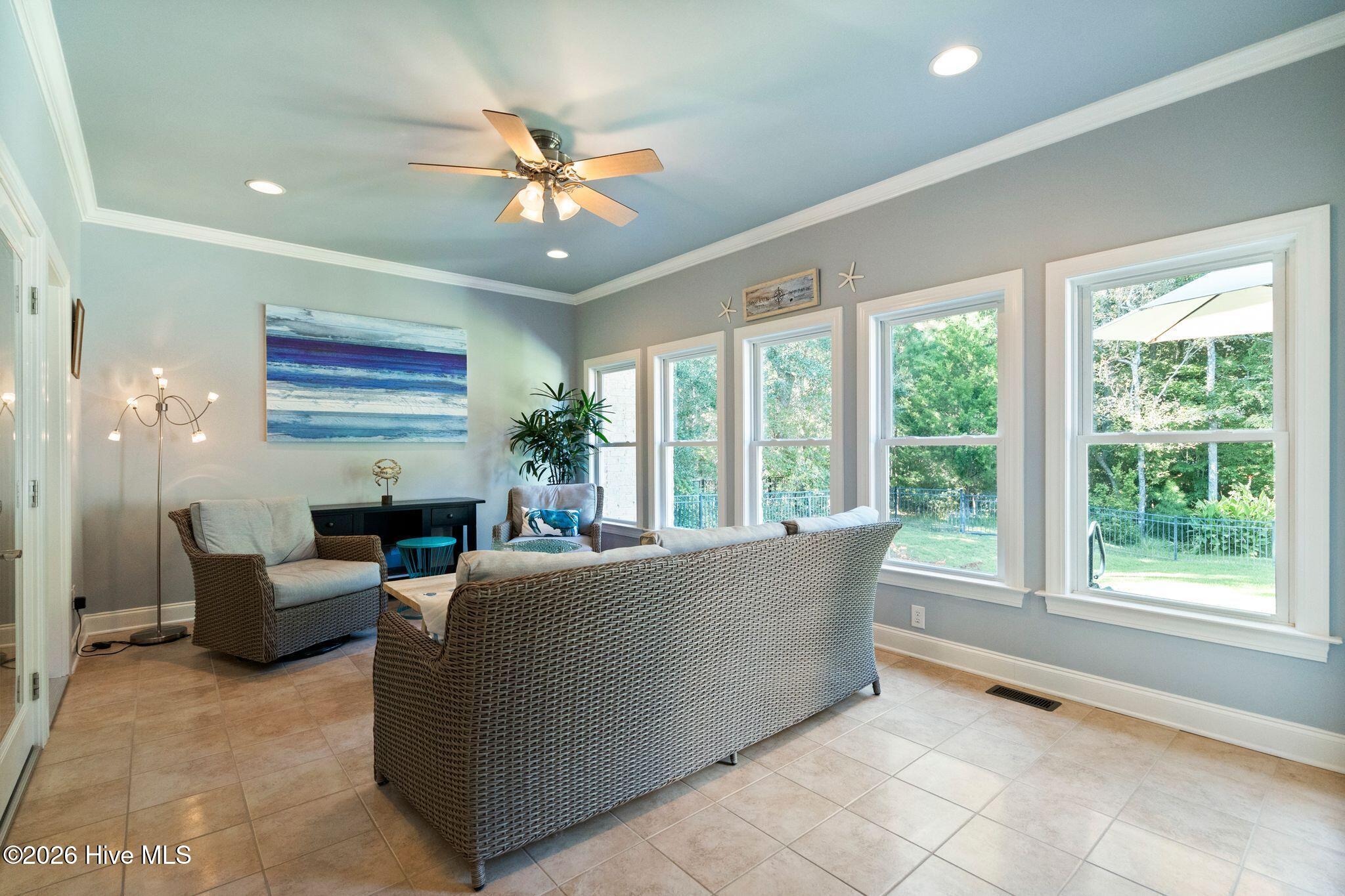 Living room with wicker seating and large windows overlooking a leafy yard.