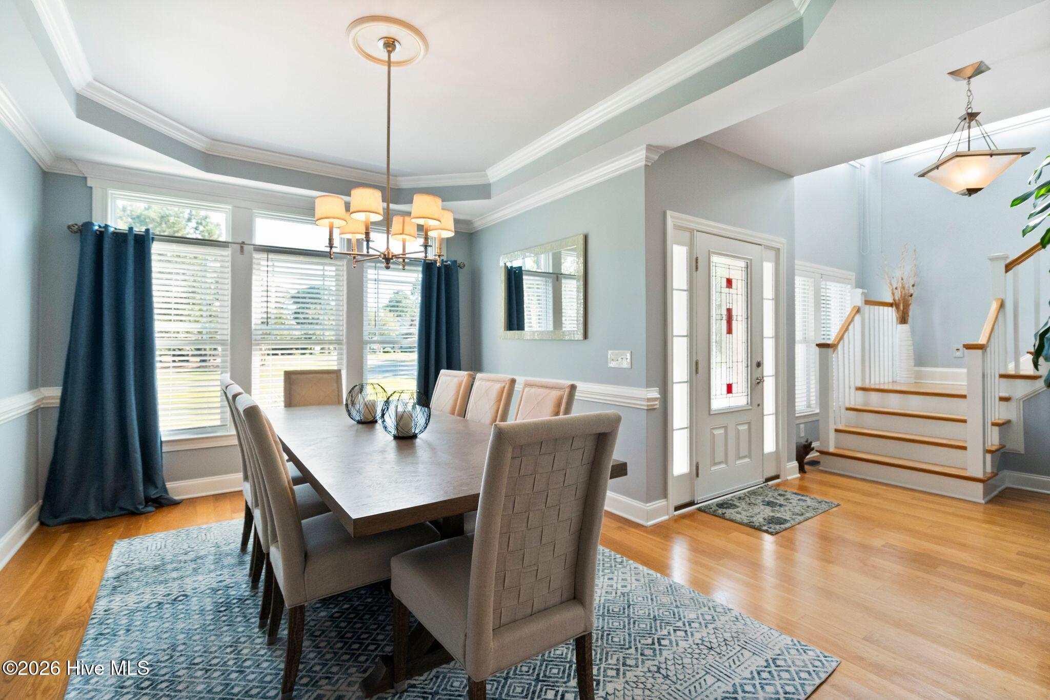 Furnished dining room with navy curtains, a long table, and a staircase beside the entry.