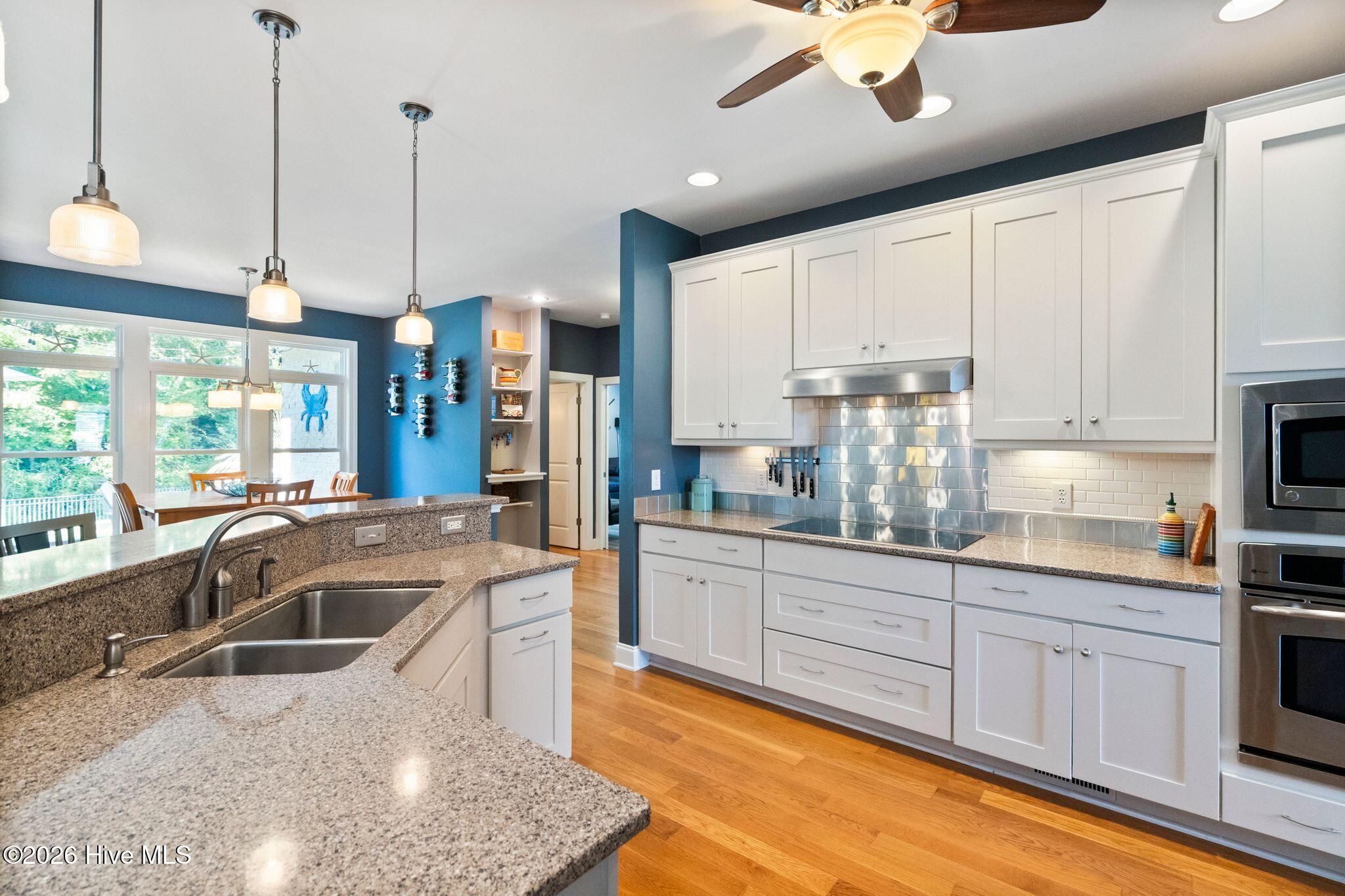 Kitchen with white cabinetry, granite island and sink, reflective tile backsplash, and adjoining windowed dining area.