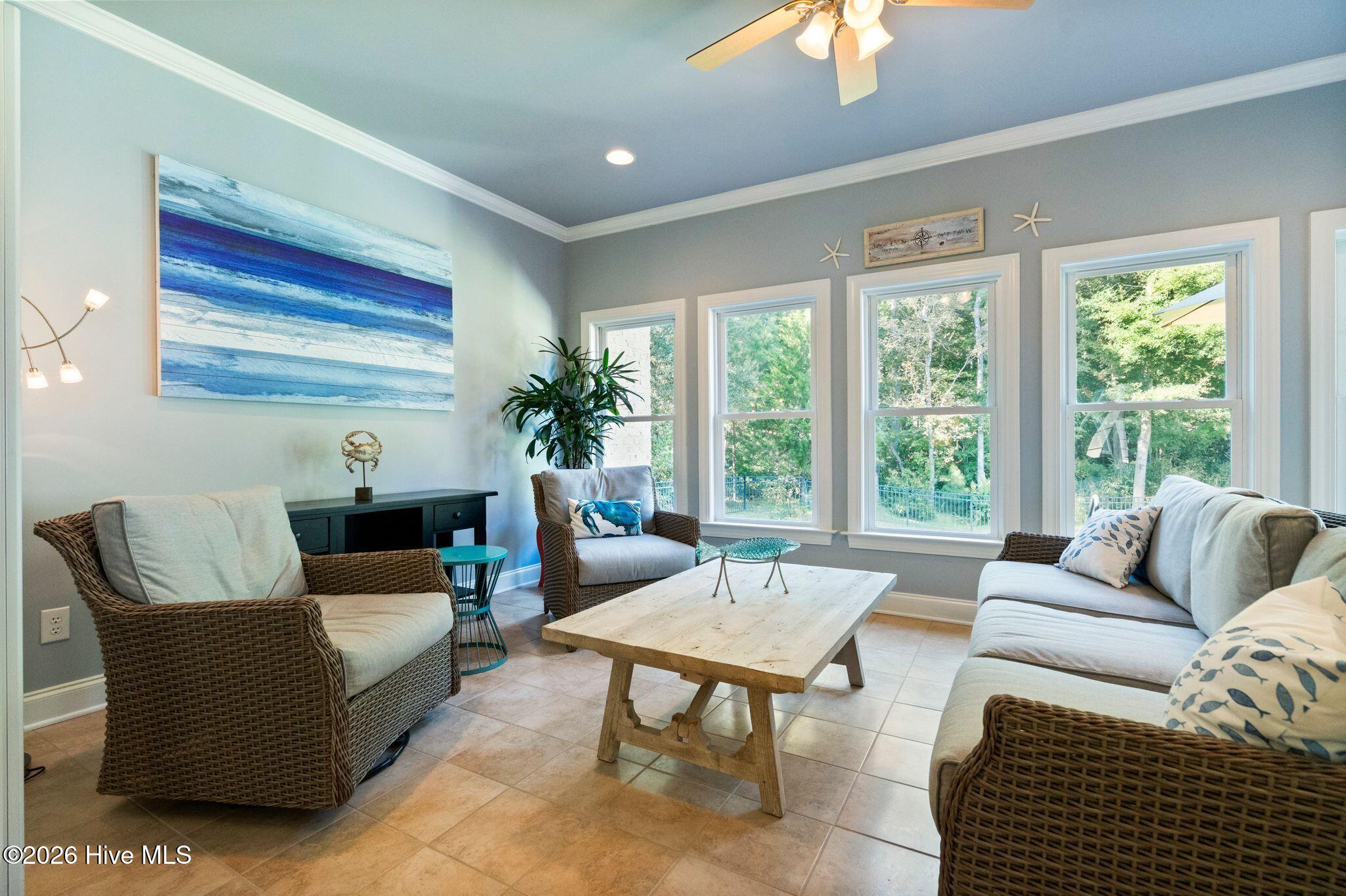 Furnished living room with wicker seating, a rustic coffee table, and large windows overlooking greenery.