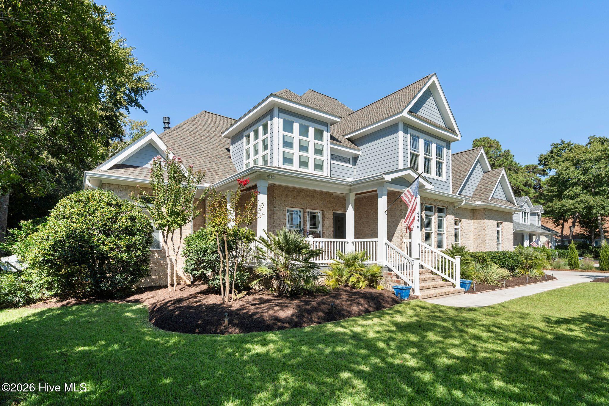 Two-story brick and gray-sided home with a covered porch, American flag, and landscaped front lawn.