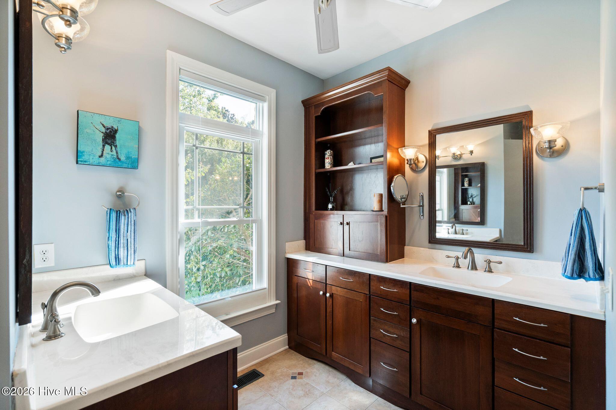 Bathroom with dual sinks, dark wood vanities, built-in shelving, and a tall window.
