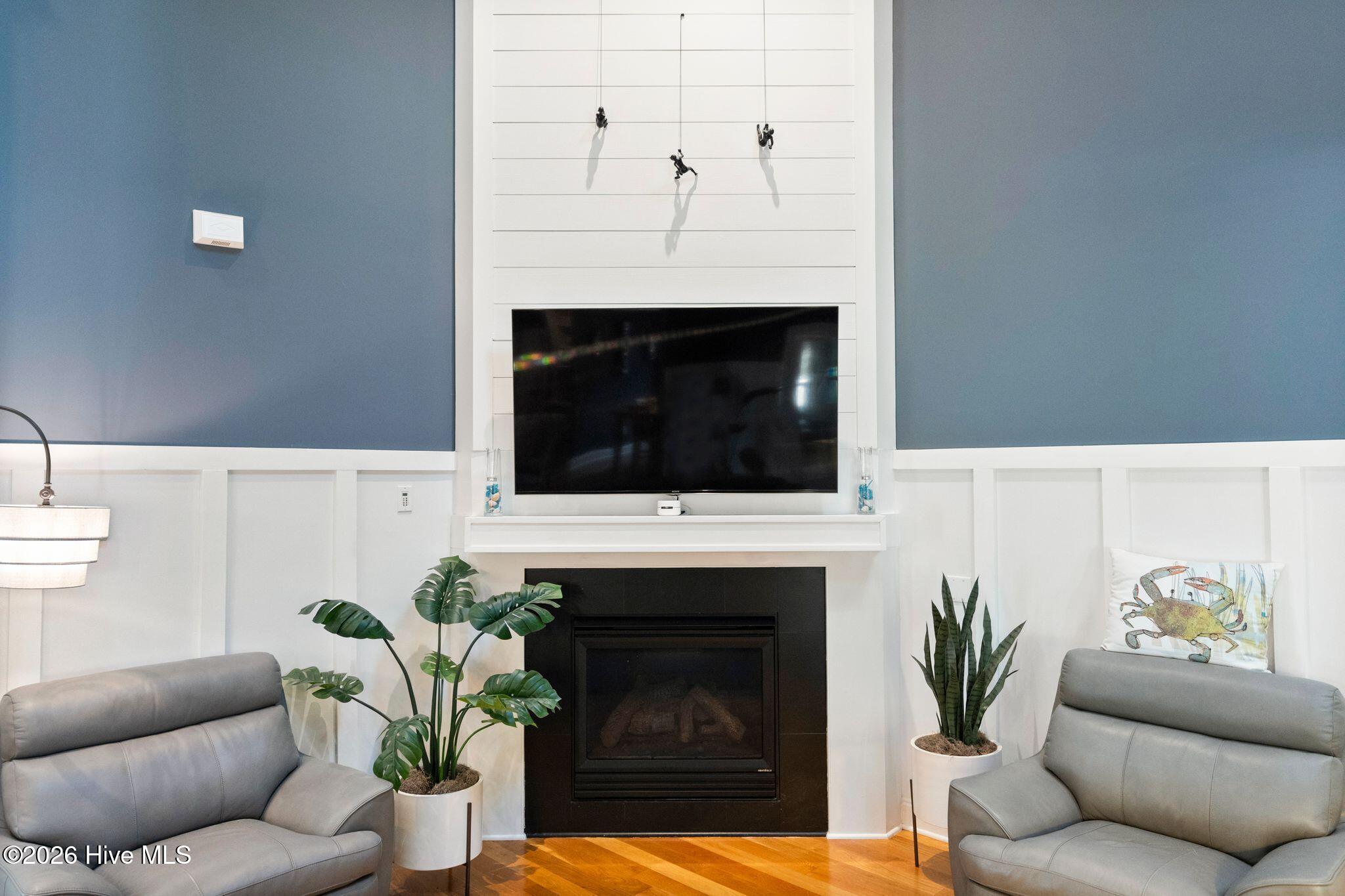Living room with a fireplace, wall-mounted TV, gray sofas, and potted plants.