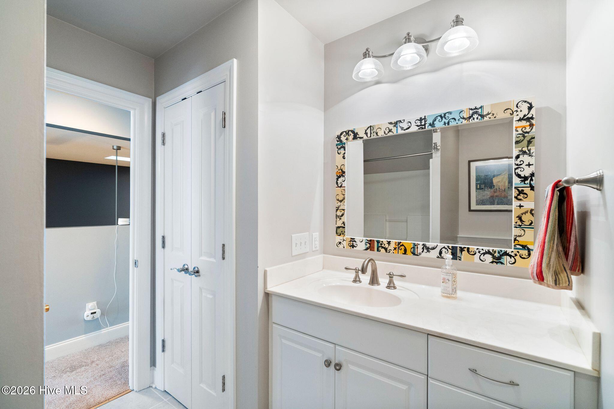 Bathroom vanity with a colorful patterned mirror frame, white countertop, and three-light fixture.