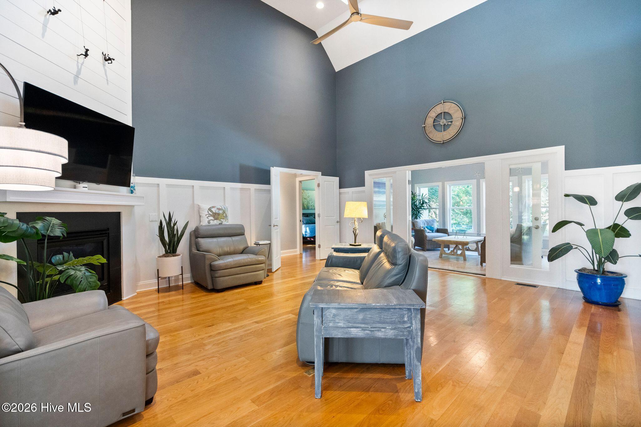 Living room with vaulted ceiling, hardwood floors, fireplace, gray seating, and glass doors to a sunroom.