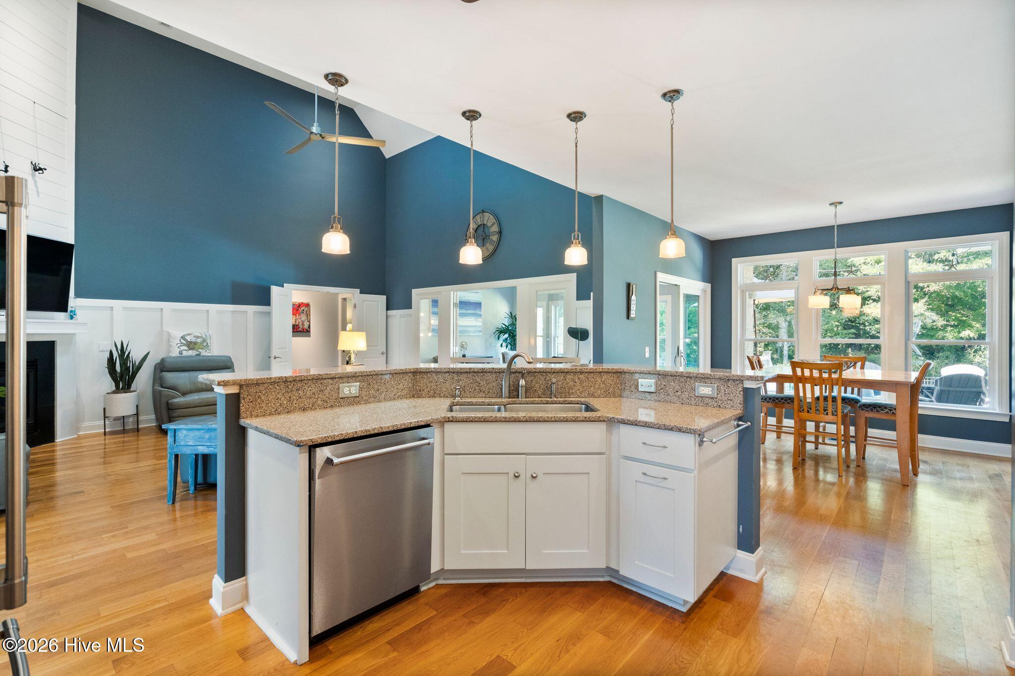 Open-plan kitchen with a granite island and stainless dishwasher, adjoining a bright dining area with large windows.