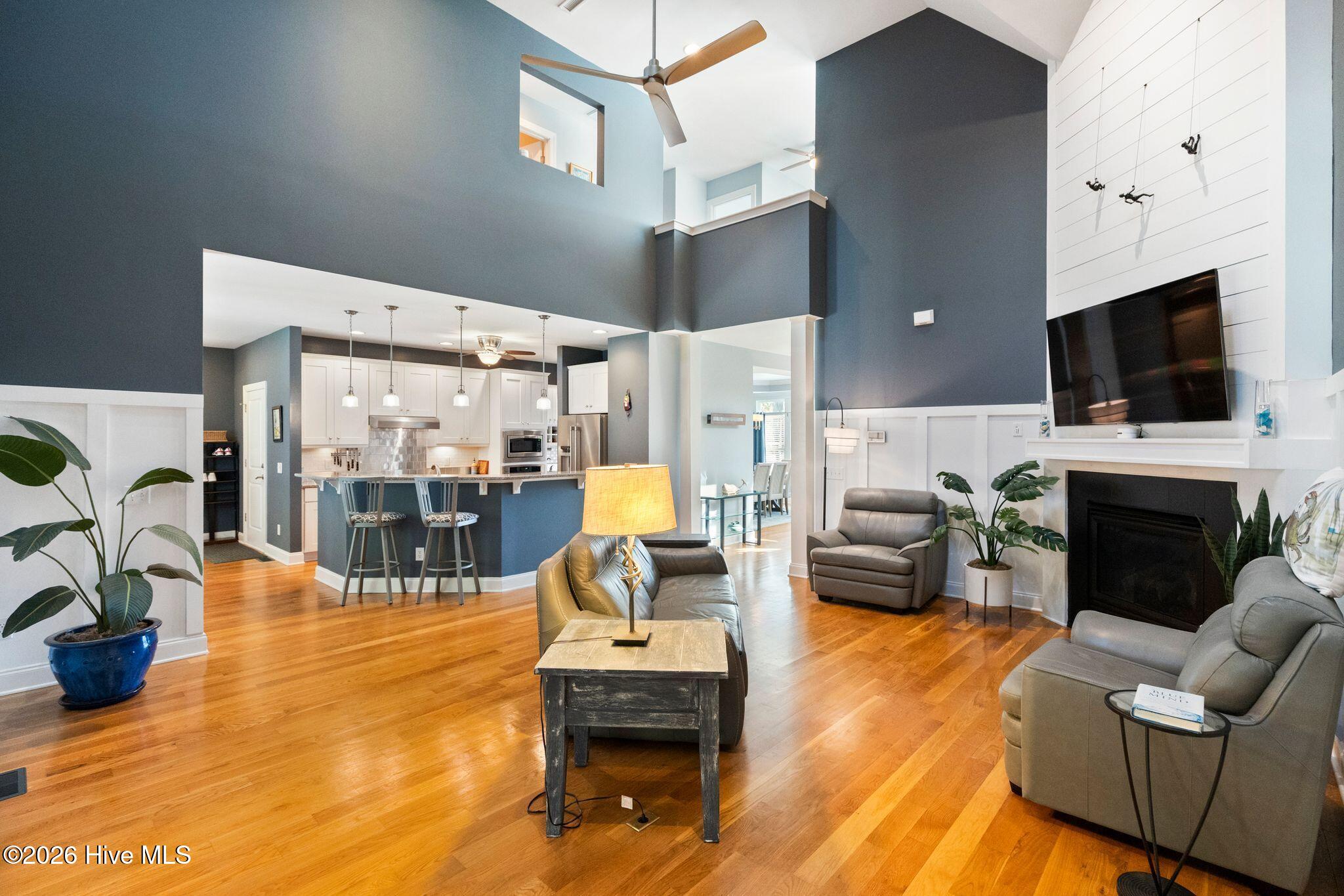 Open-plan living room and kitchen with vaulted ceilings, hardwood floors, fireplace, and breakfast bar.