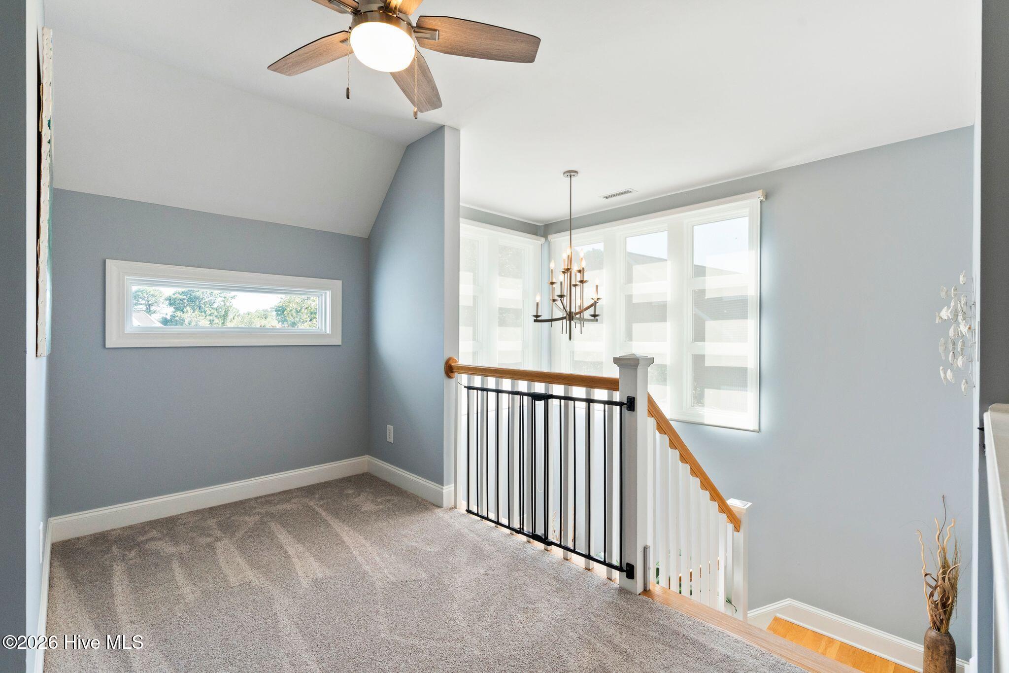 Upstairs landing with gray carpet, a ceiling fan, and a wood-and-black stair railing beside tall windows.