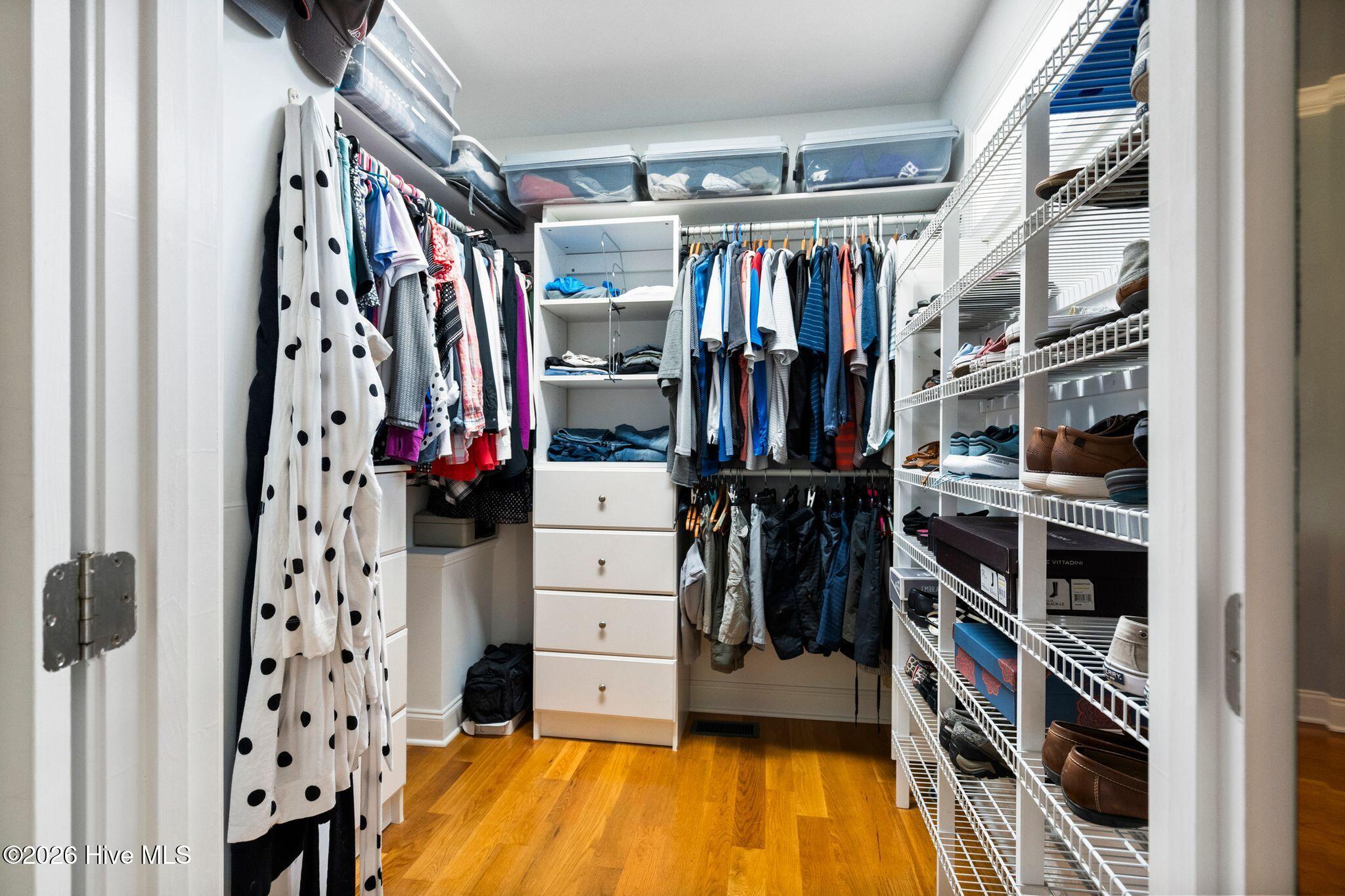 Walk-in closet with built-in drawers, hanging clothes, and extensive shoe shelving.
