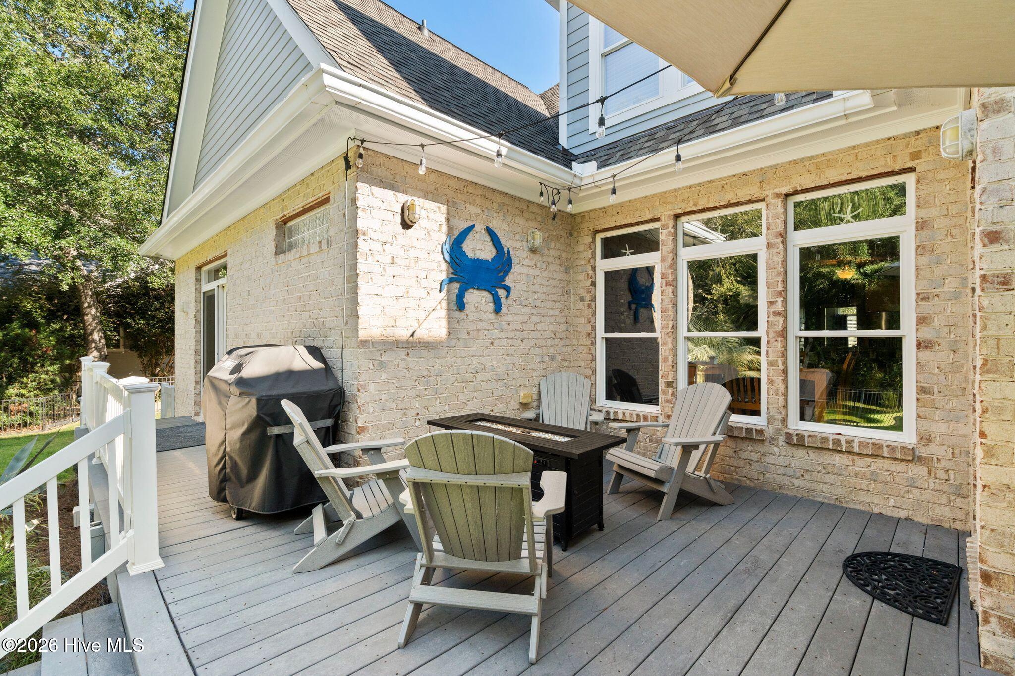 Furnished gray deck with Adirondack chairs, outdoor dining table, covered grill, and blue crab wall decoration.