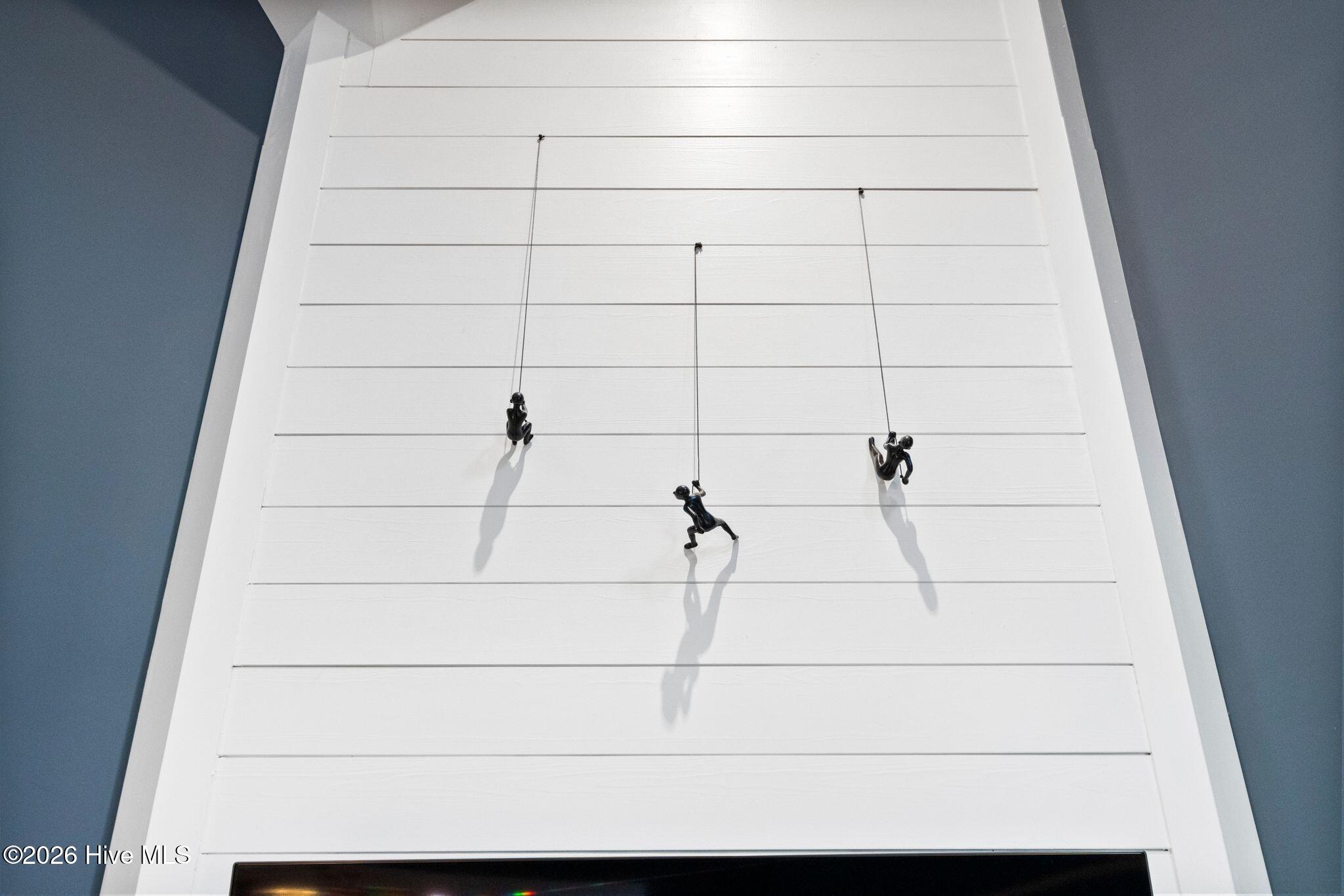 Three black climbing-figure sculptures hang on white paneling above a television.