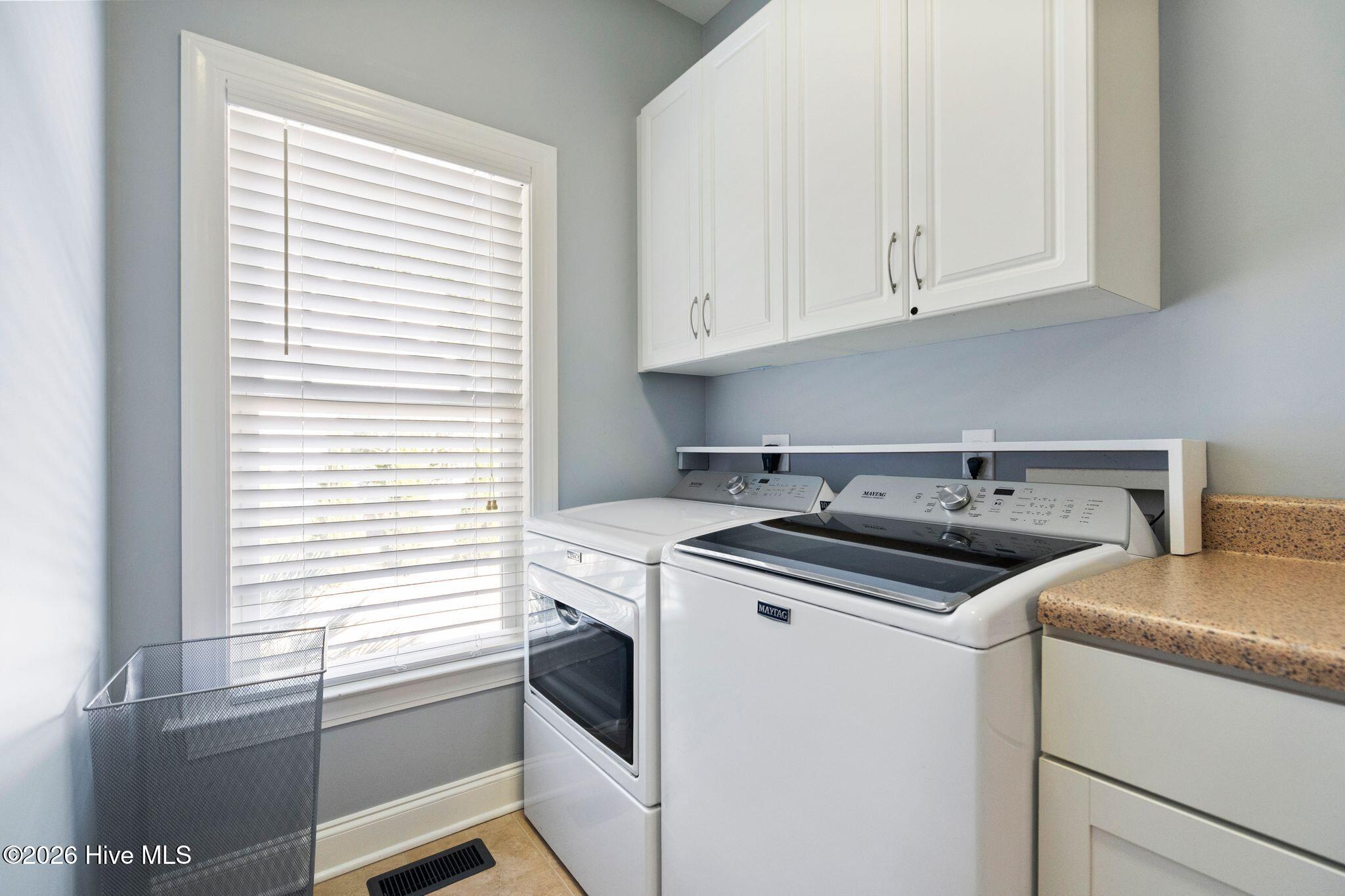 Laundry room with Maytag washer and dryer, white cabinets, and a window with blinds.