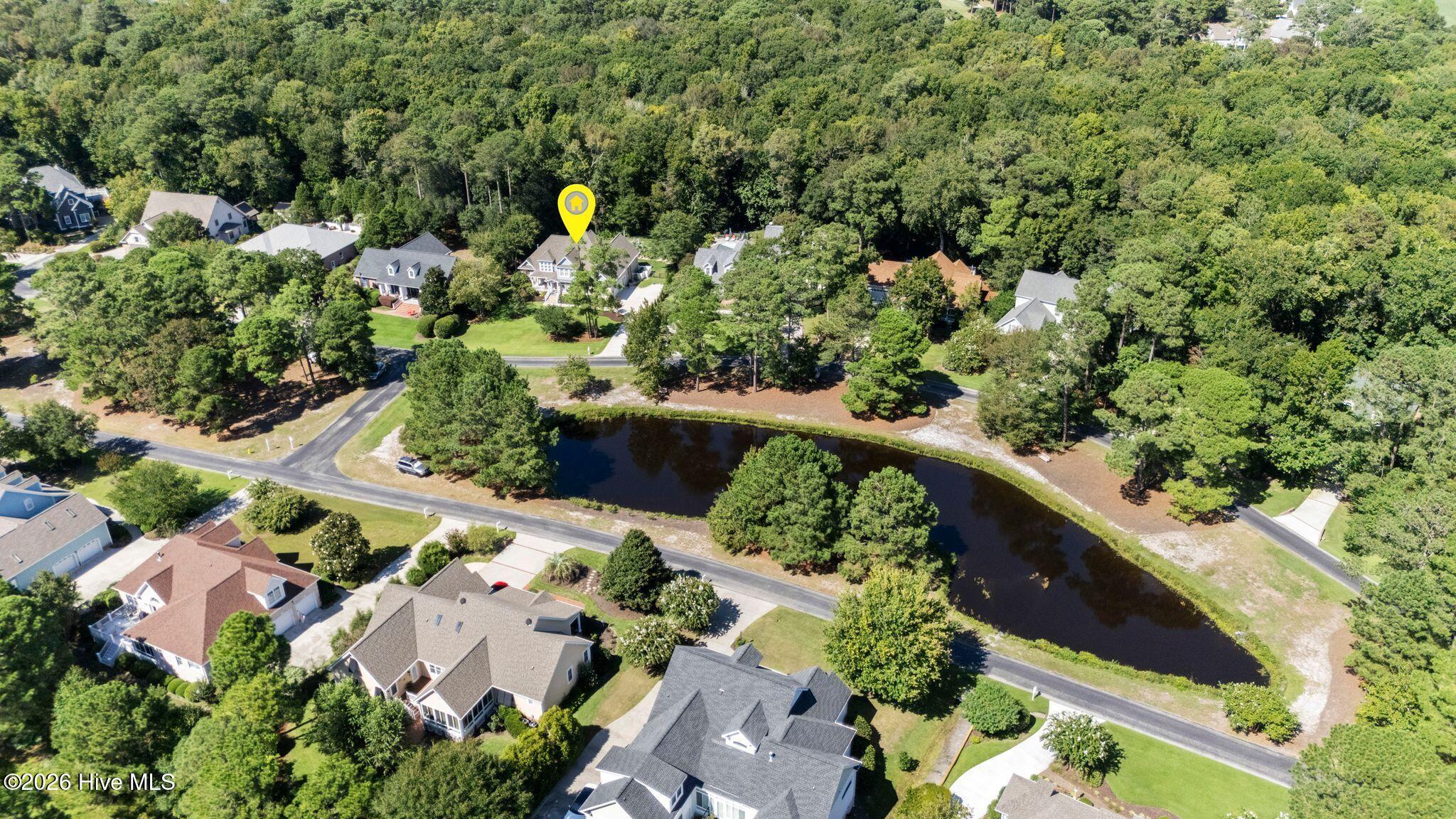 Aerial view of the home beside a pond, surrounded by mature trees and neighboring houses.