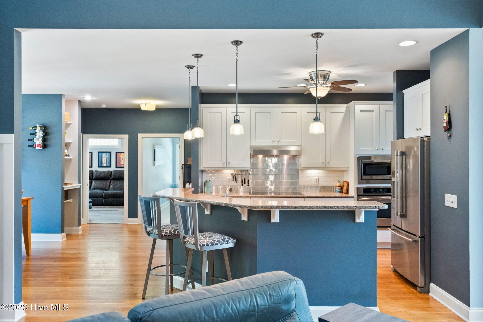 Open-plan kitchen with a blue breakfast island, white cabinets, stainless steel appliances, and hardwood floors.