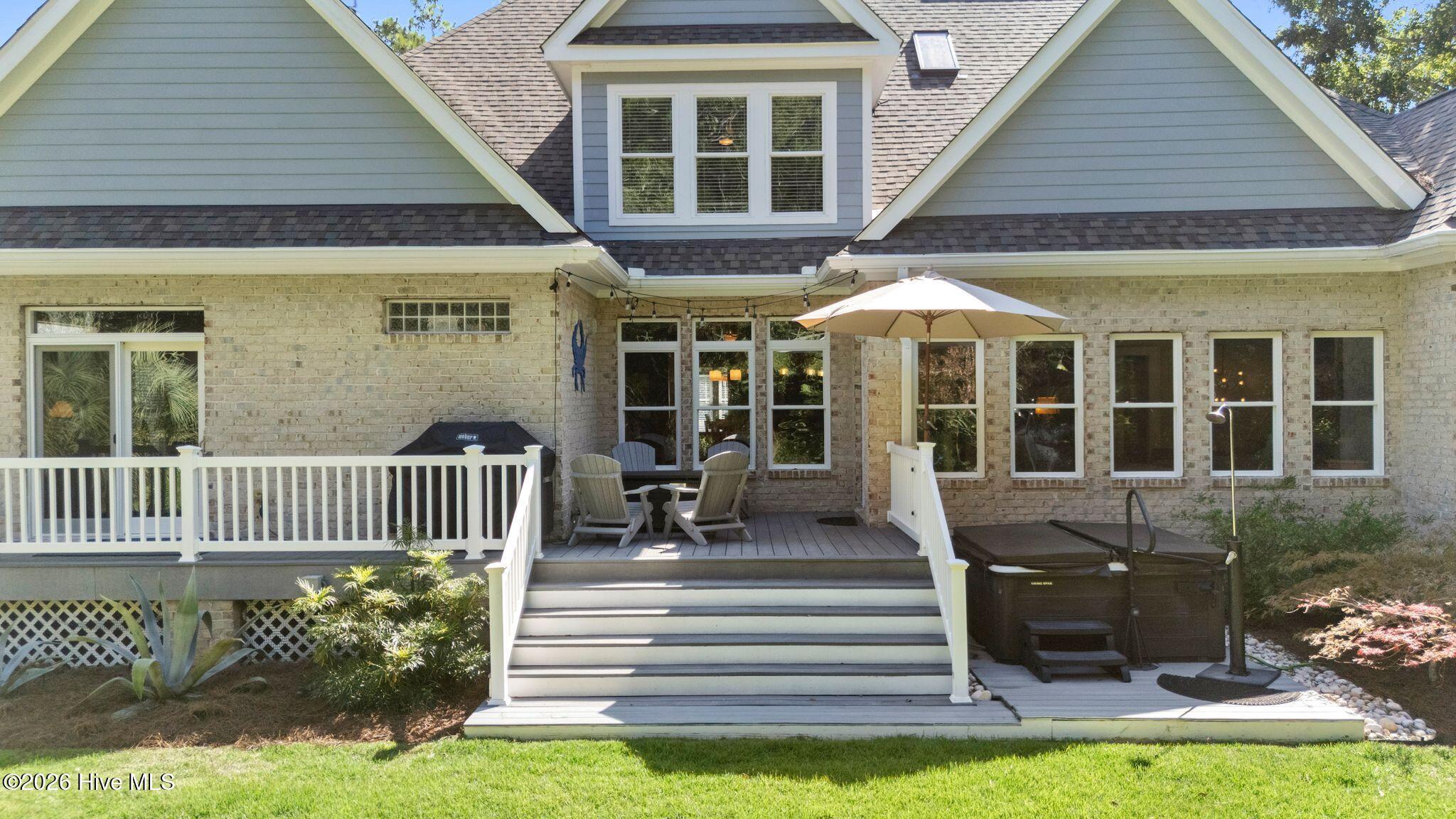 Rear of a brick house with a raised deck, outdoor seating, umbrella, and covered hot tub.