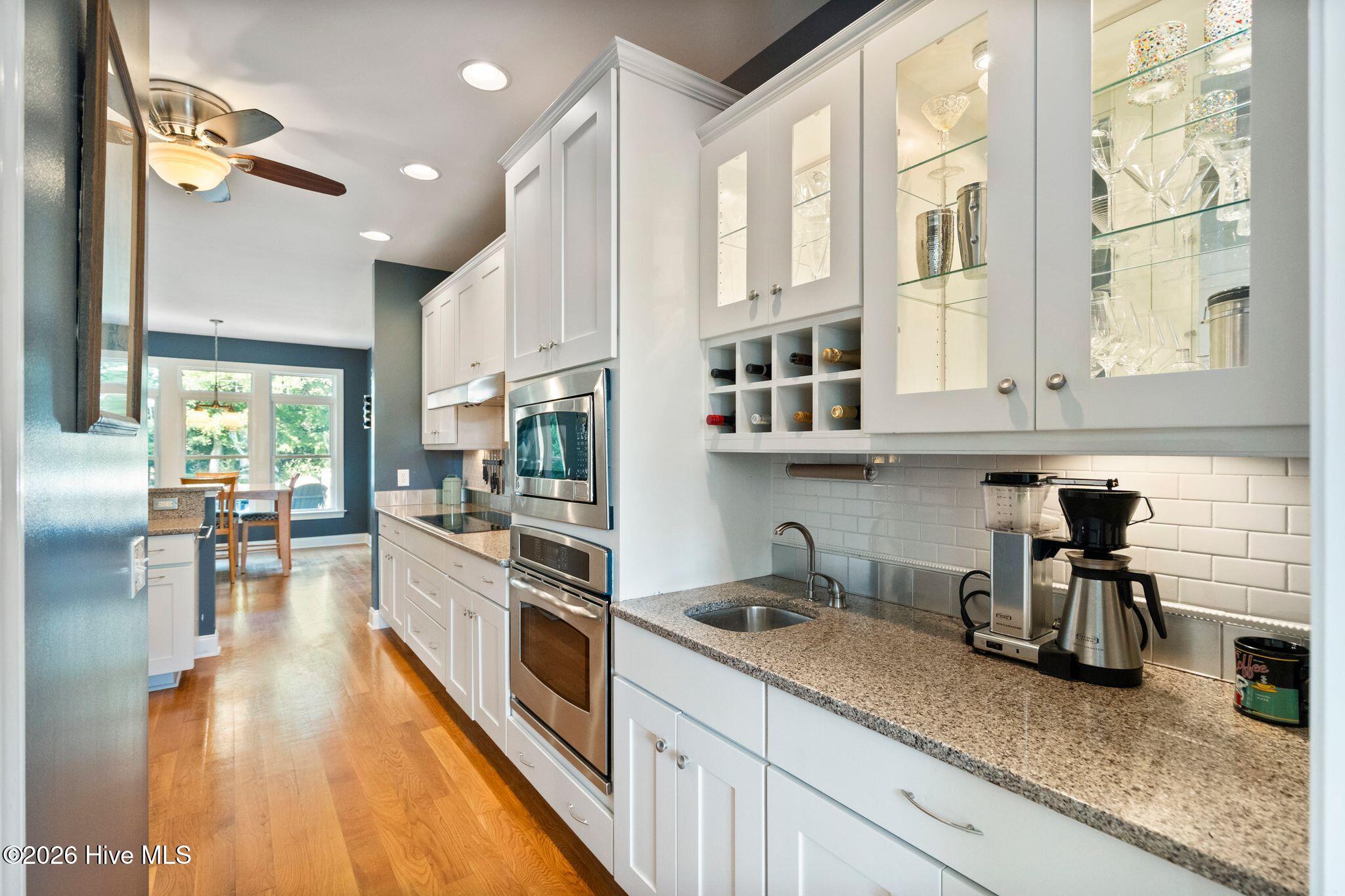 Kitchen with white glass-front cabinets, granite counters, stainless appliances, and hardwood floors.