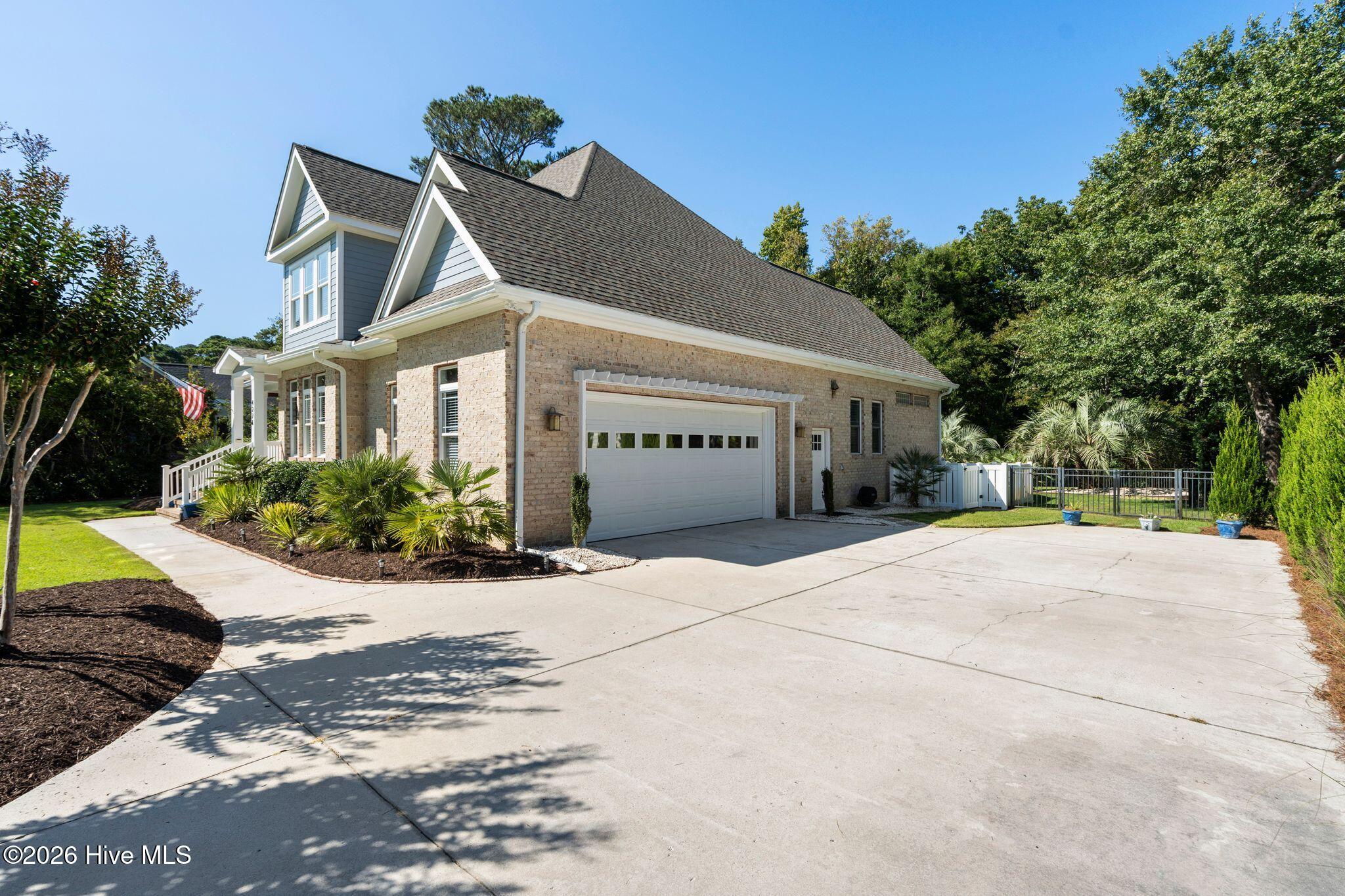 Two-story brick house with a white double garage door, broad driveway, landscaped palms, and an American flag.