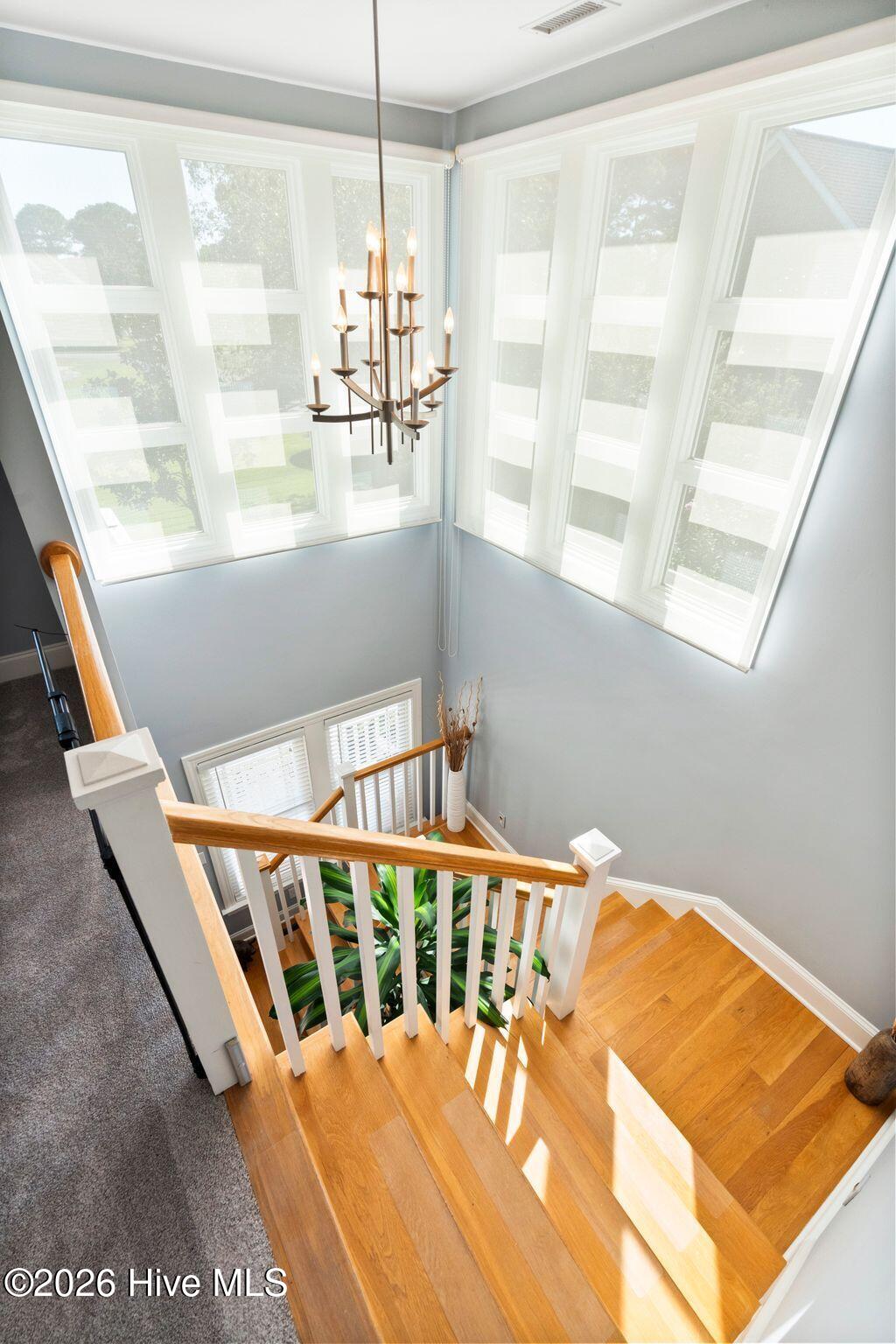 Wood staircase with white balusters beneath tall windows and a branching chandelier.