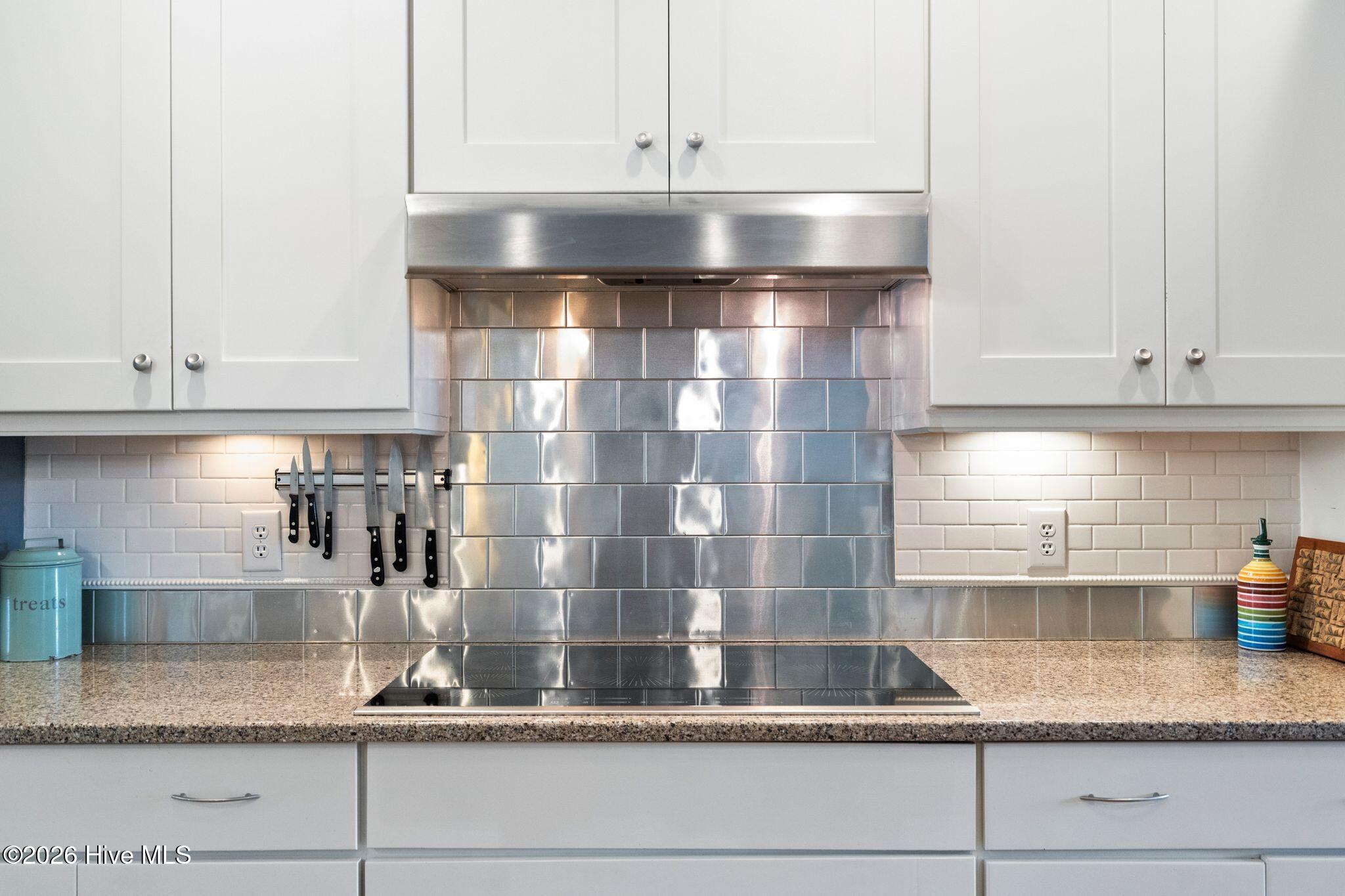 Kitchen with reflective metal tile backsplash, stainless steel range hood, and granite countertop.