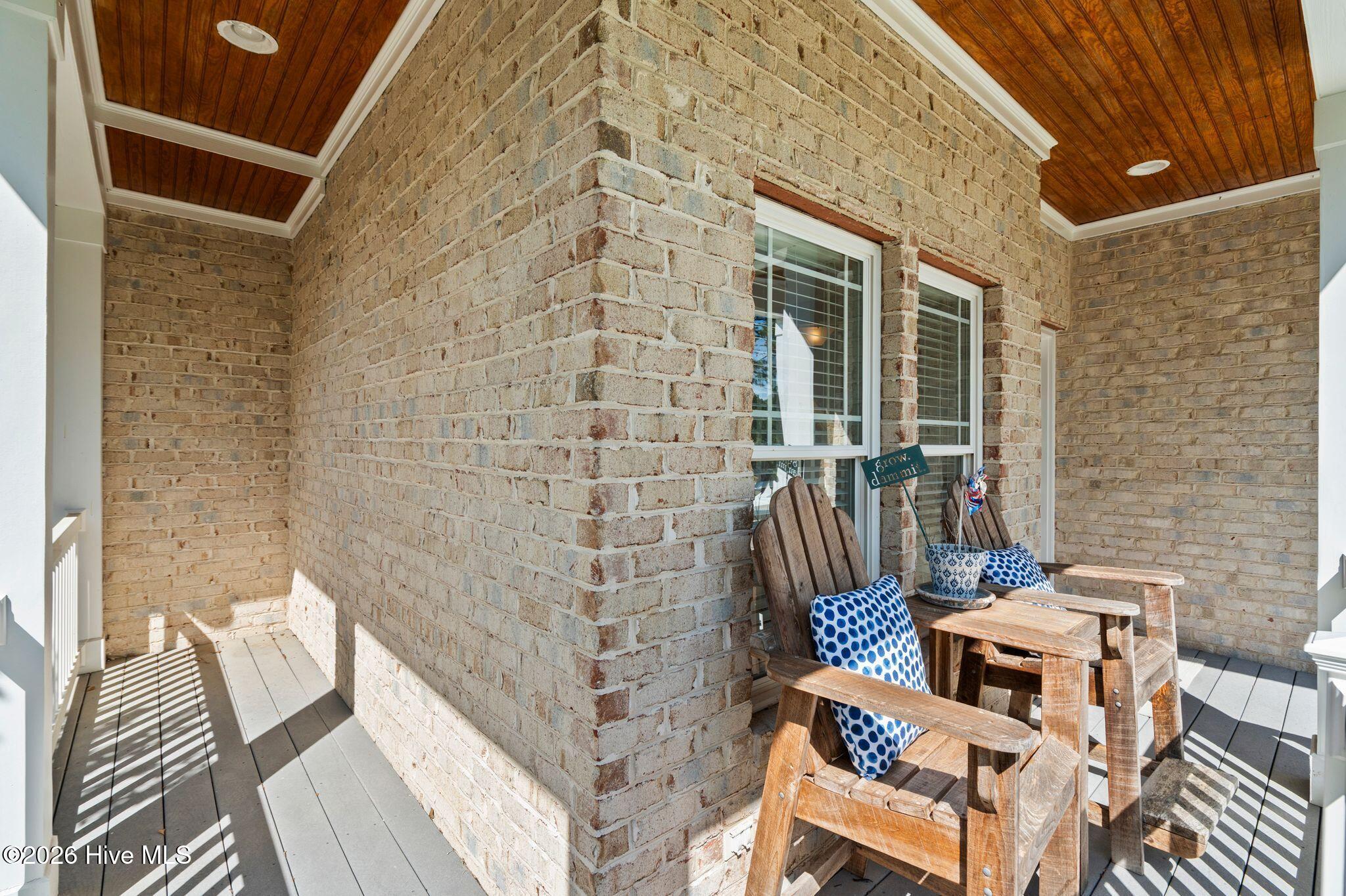 Covered brick porch with a wood ceiling and two Adirondack chairs with blue-and-white cushions.