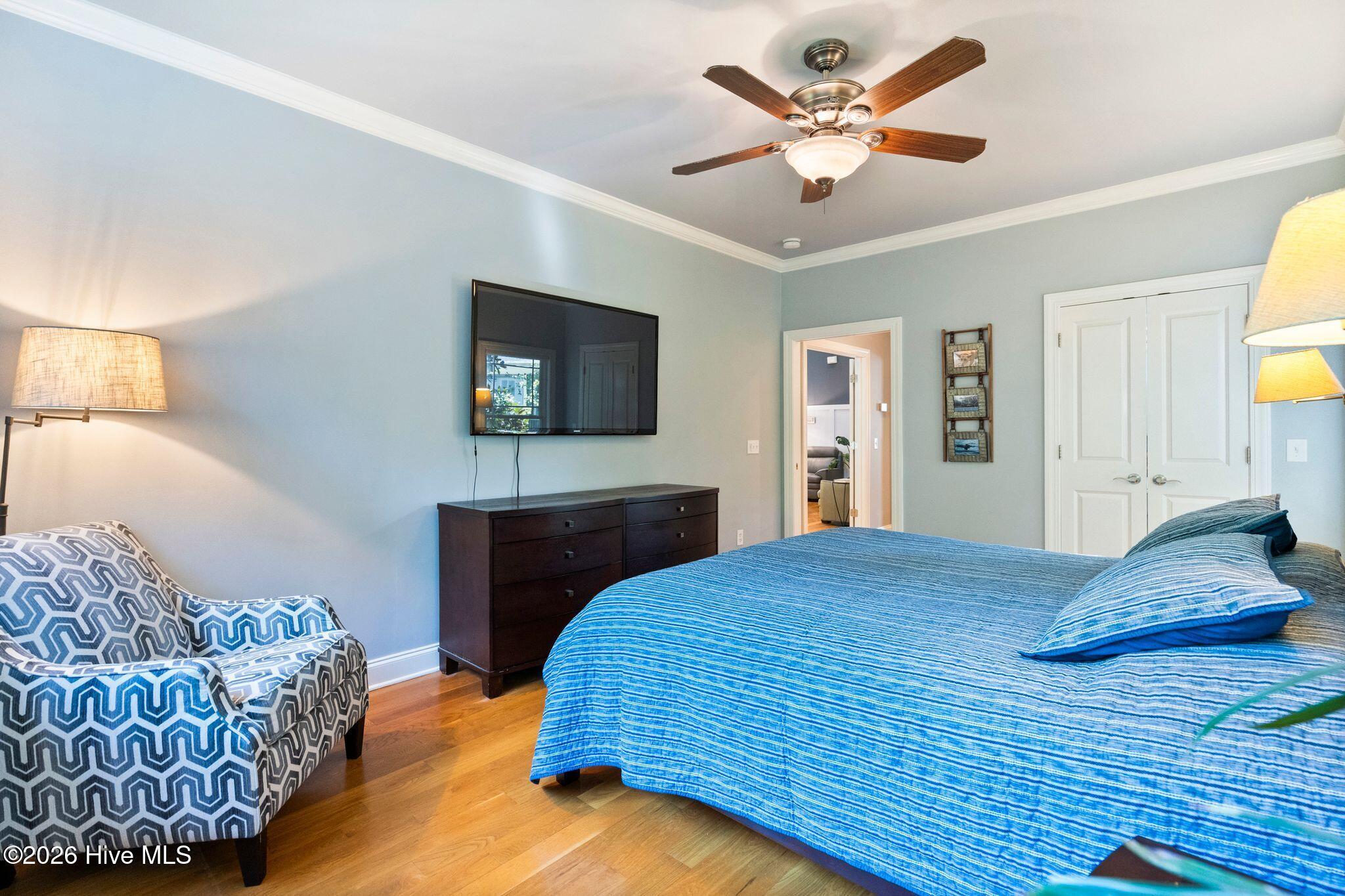 Bedroom with a blue-striped bed, patterned armchair, wall-mounted TV, and ceiling fan.