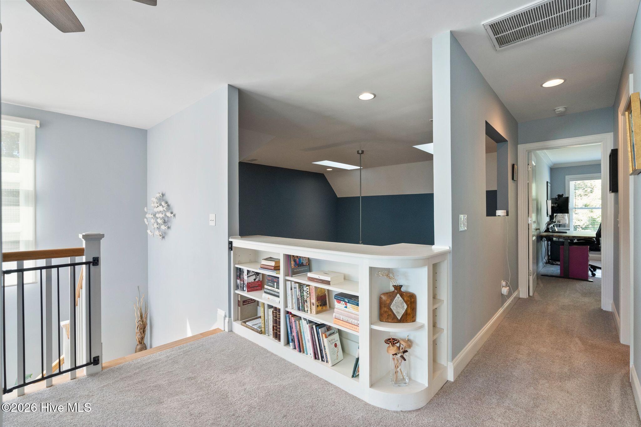 Upstairs landing with a built-in bookcase, stair railing, and hallway leading to a home office.