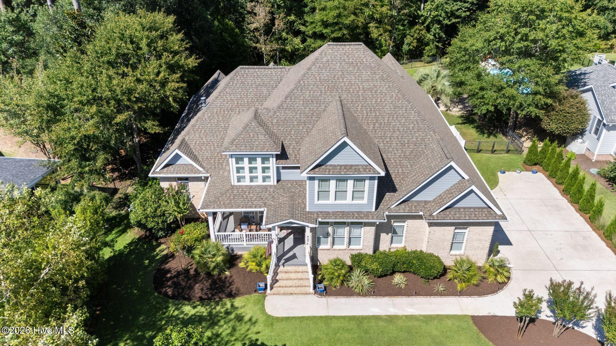 Aerial view of a brick-and-gray home with a complex roof, front porch, landscaped yard, and curved driveway.