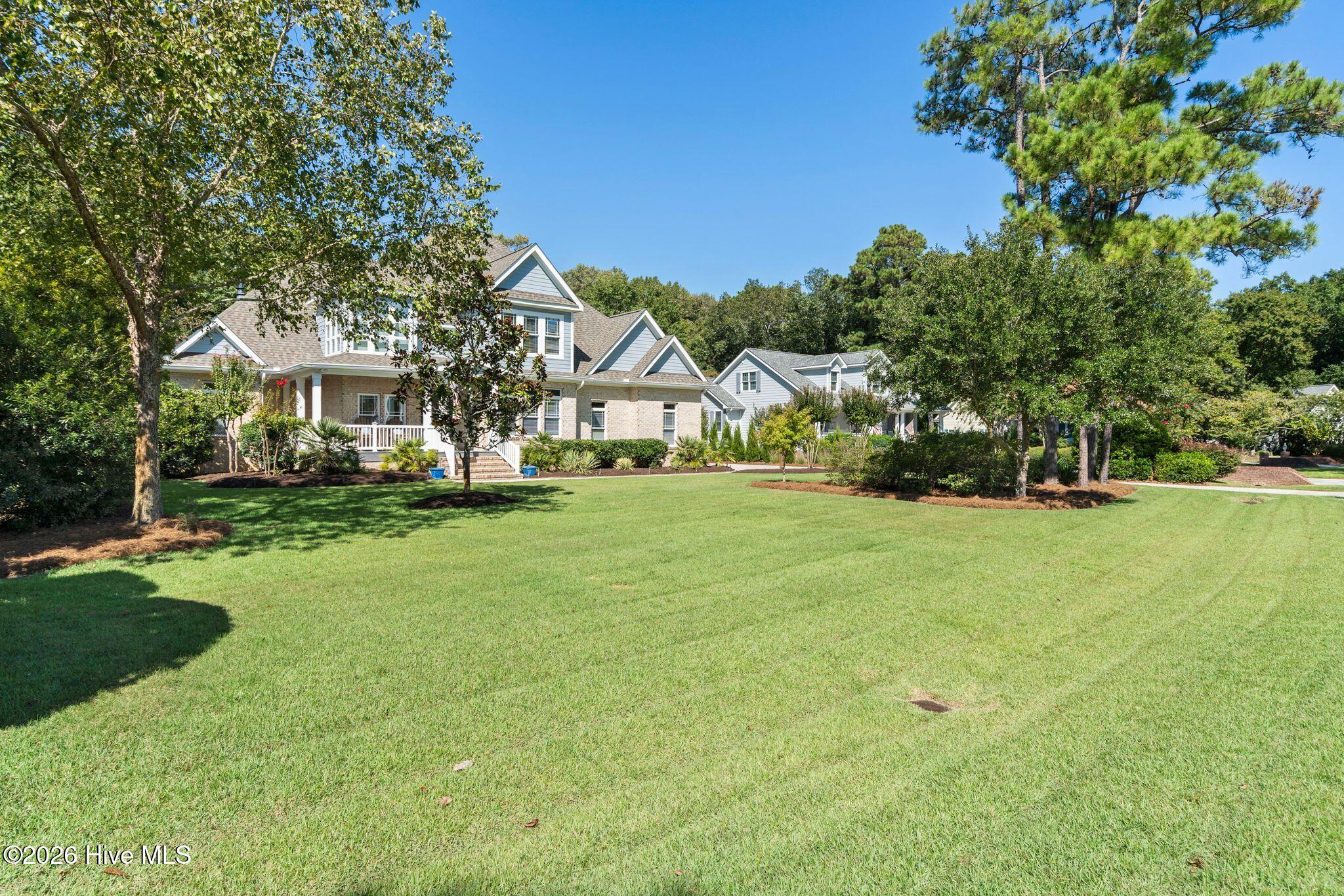 Two-story brick and blue-gray home with a covered porch, broad lawn, and mature trees.