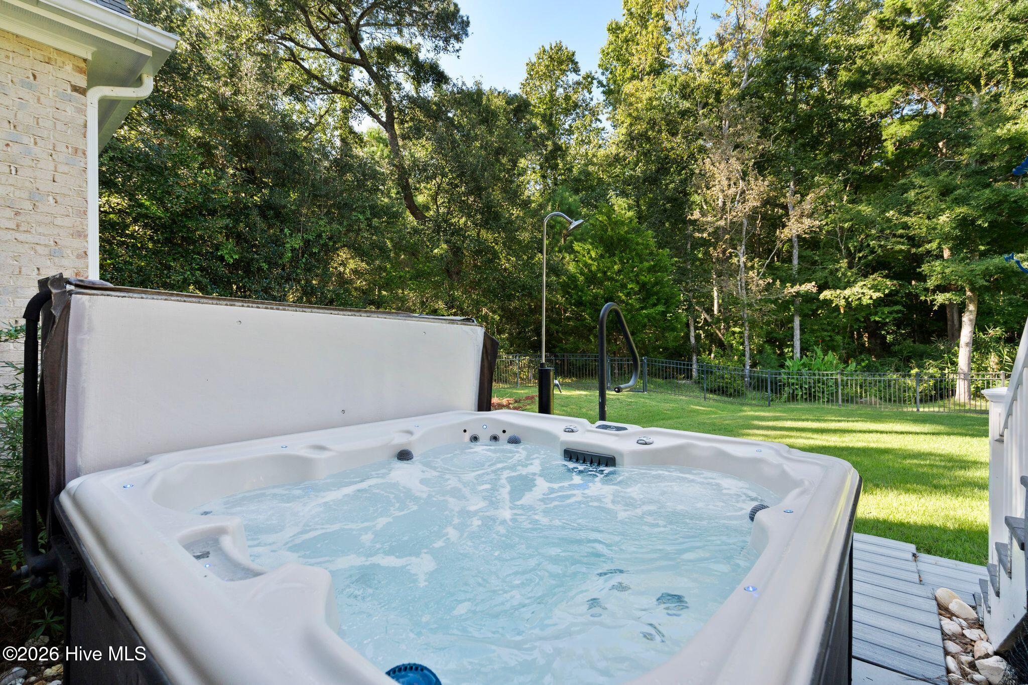 Outdoor hot tub beside a grassy, wooded backyard.