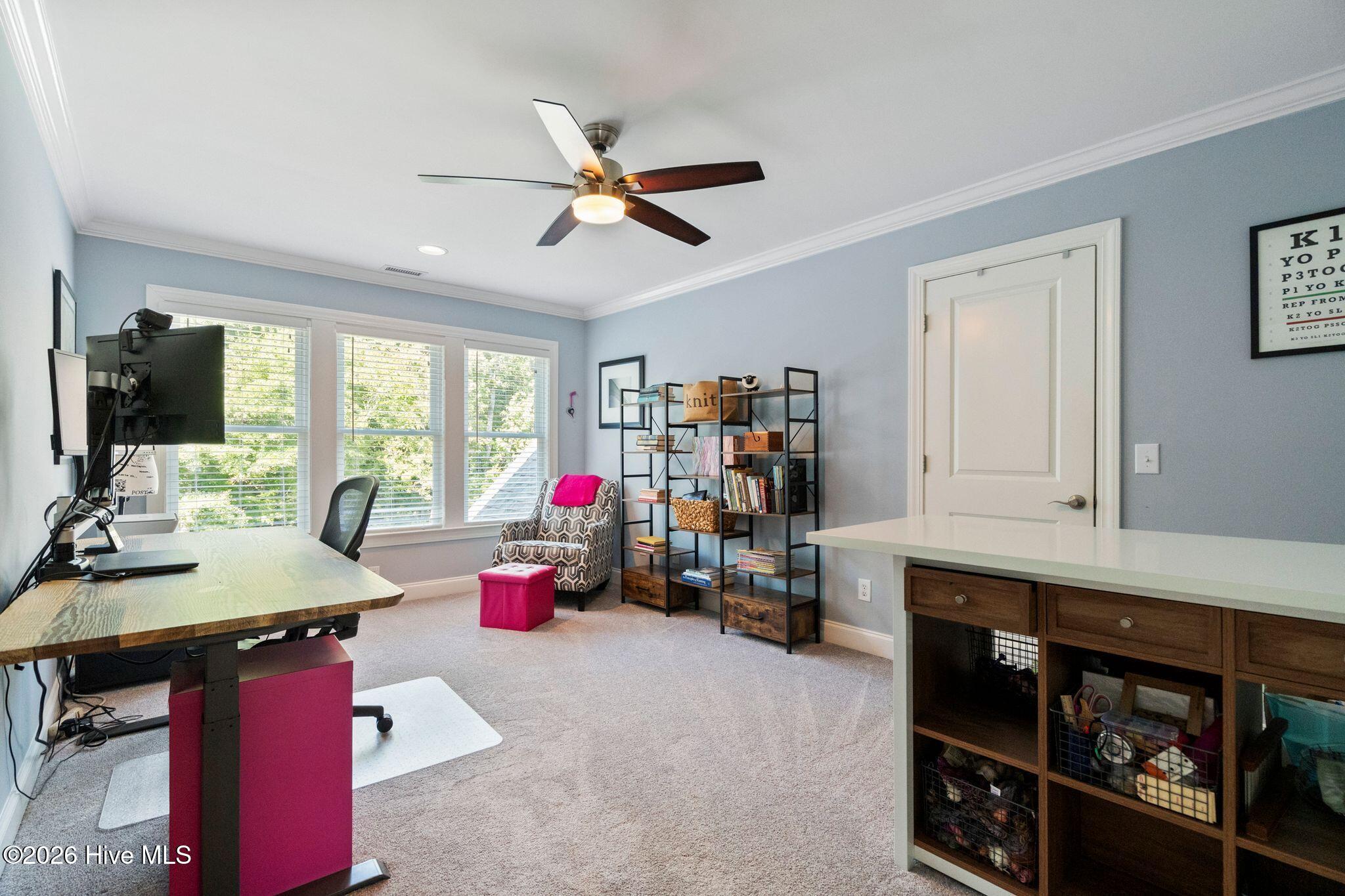 Furnished home office with three bright windows, open shelving, and a built-in desk.