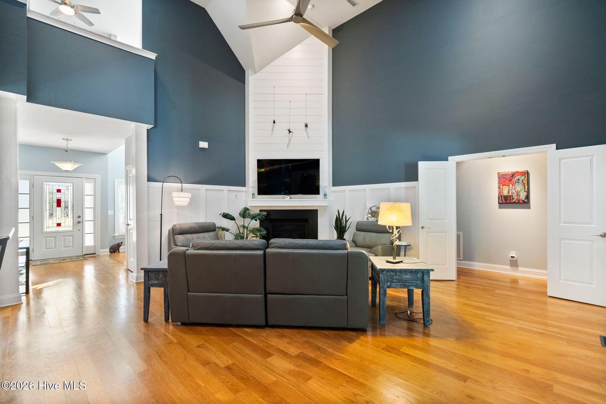 Living room with vaulted ceiling, blue walls, hardwood floors, and a fireplace beneath a television.