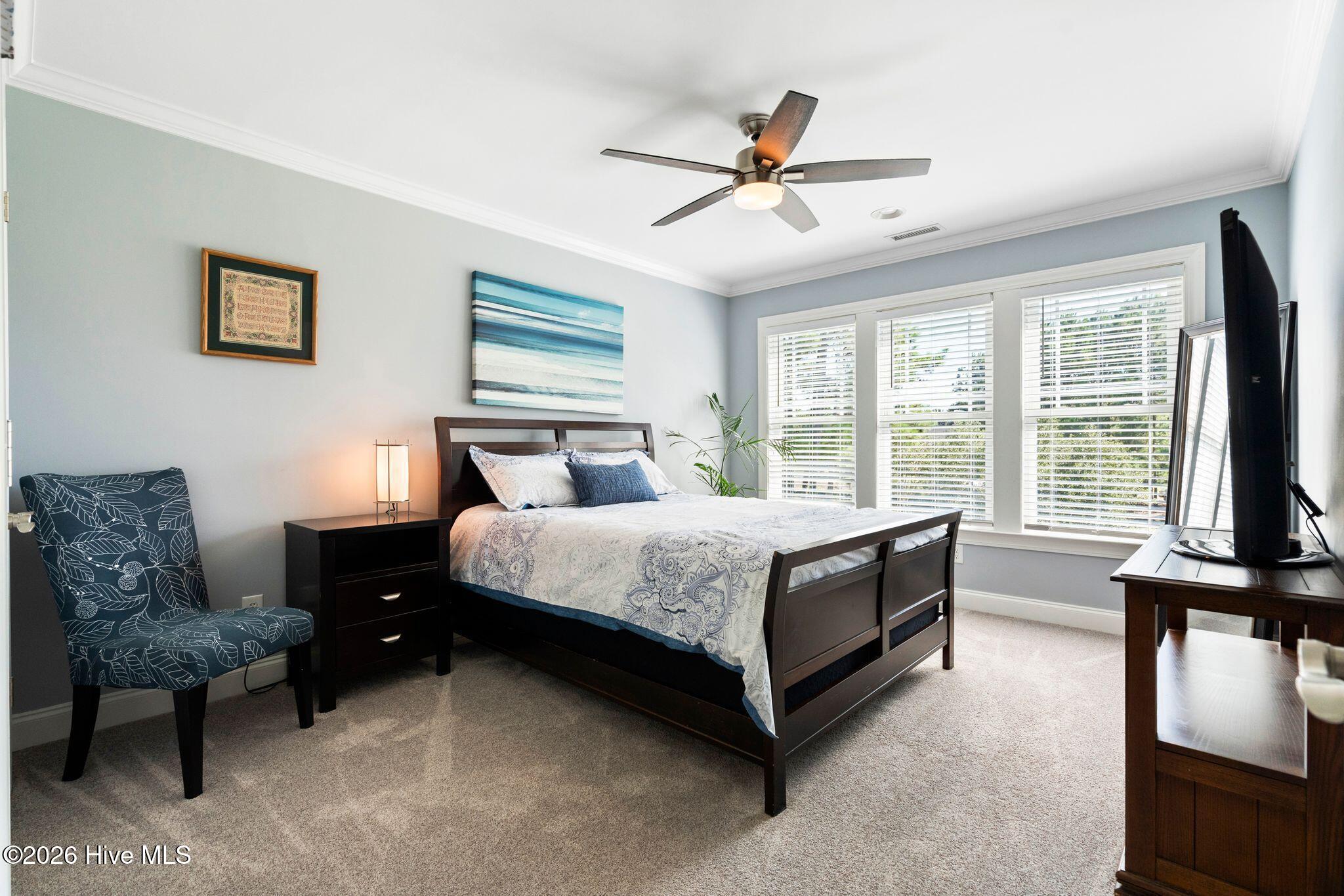 Furnished bedroom with a dark wood bed, blue accent chair, and wide windows with white blinds.