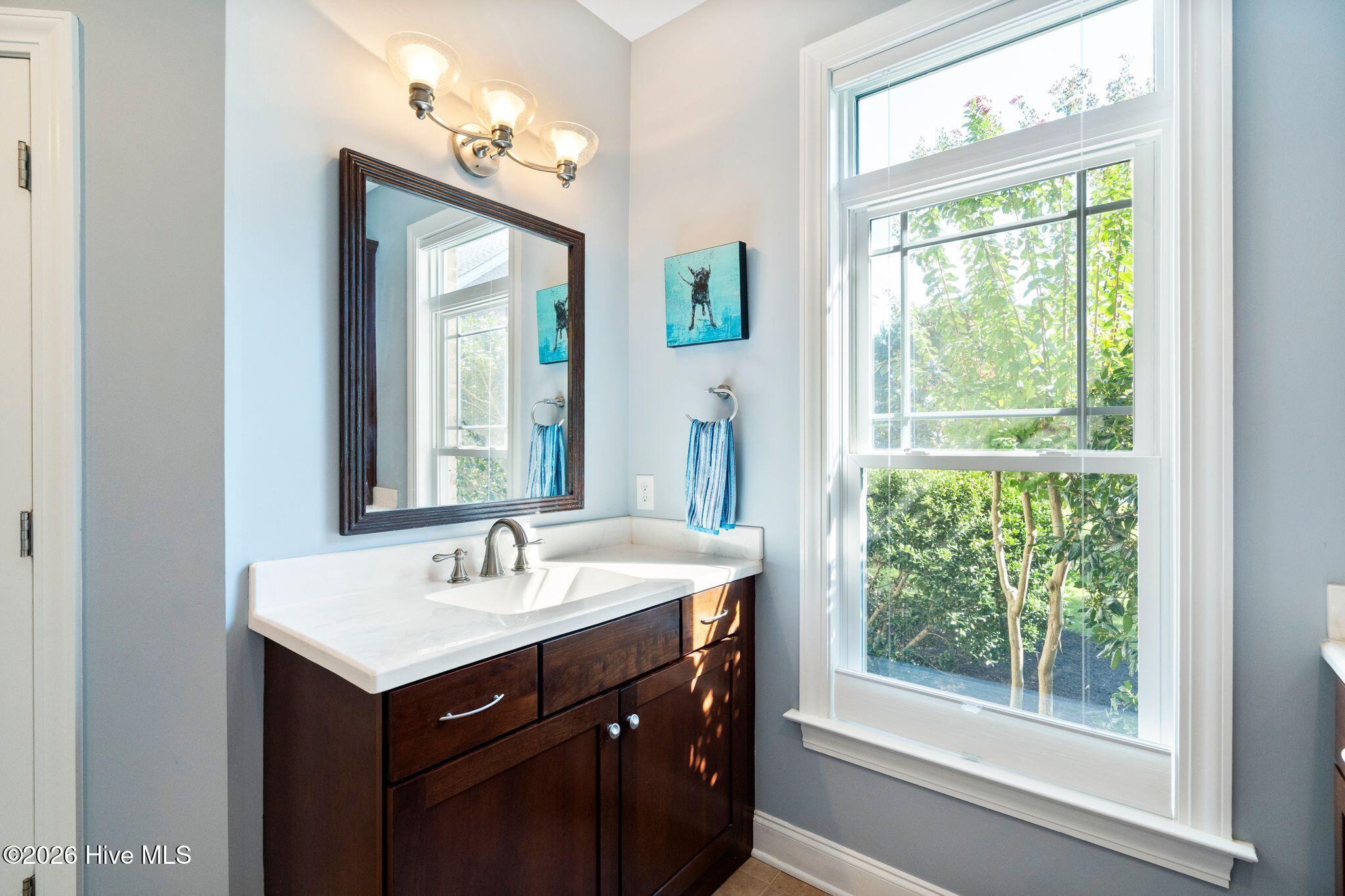 Bathroom vanity with dark wood cabinetry, white countertop, framed mirror, and a large window overlooking trees.