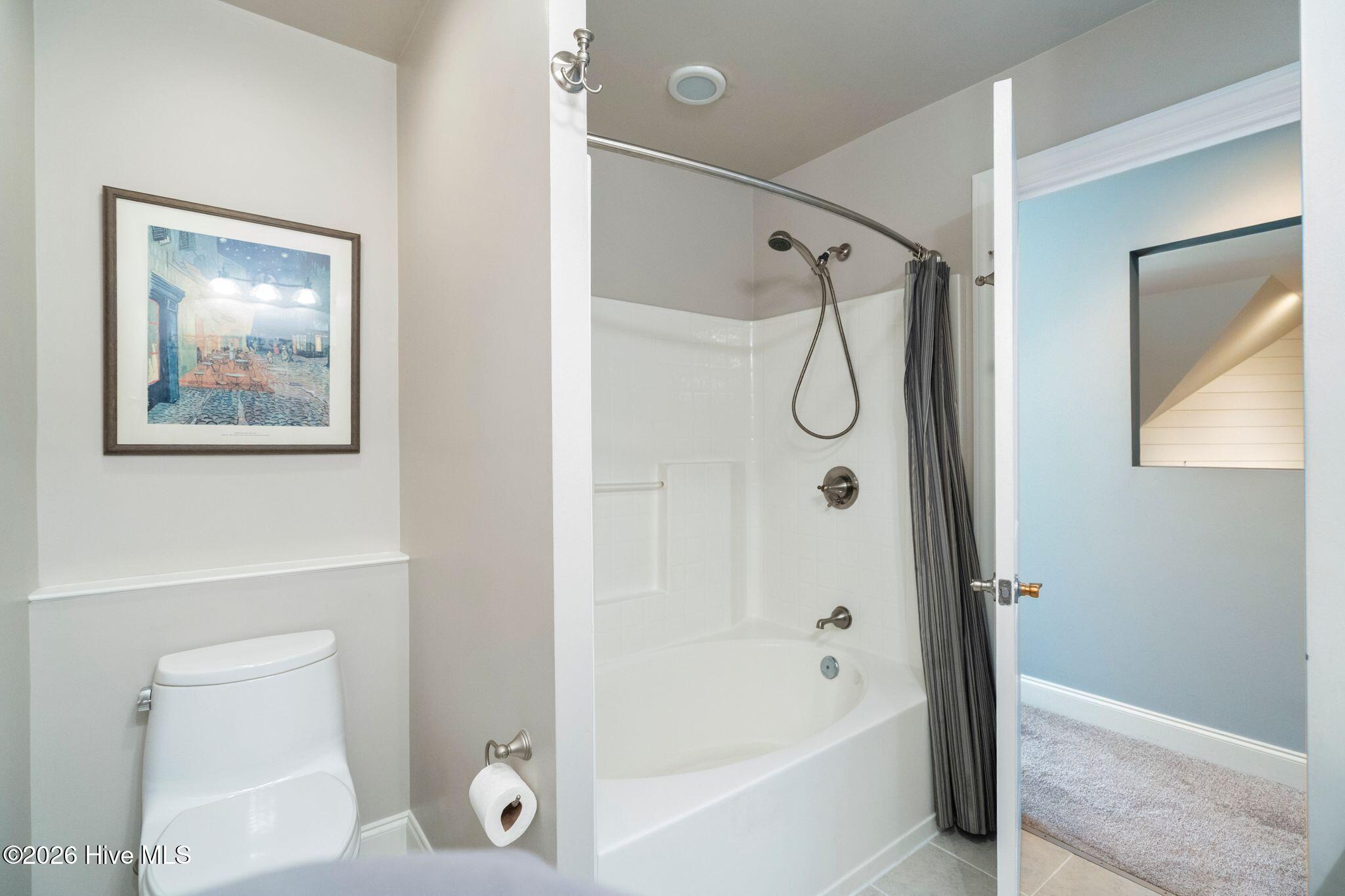 Bathroom with a white tub-shower, dark striped curtain, and framed artwork above the toilet.