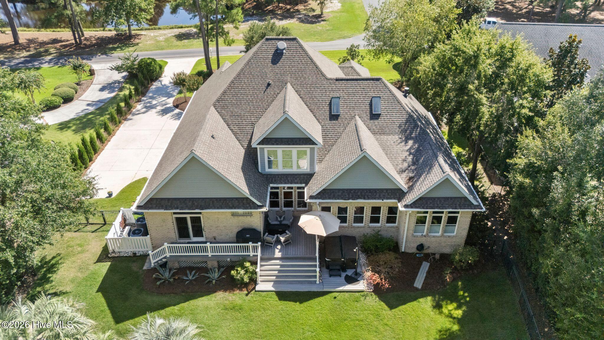 Aerial view of a brick home’s rear, with a multi-gabled roof and furnished raised deck.