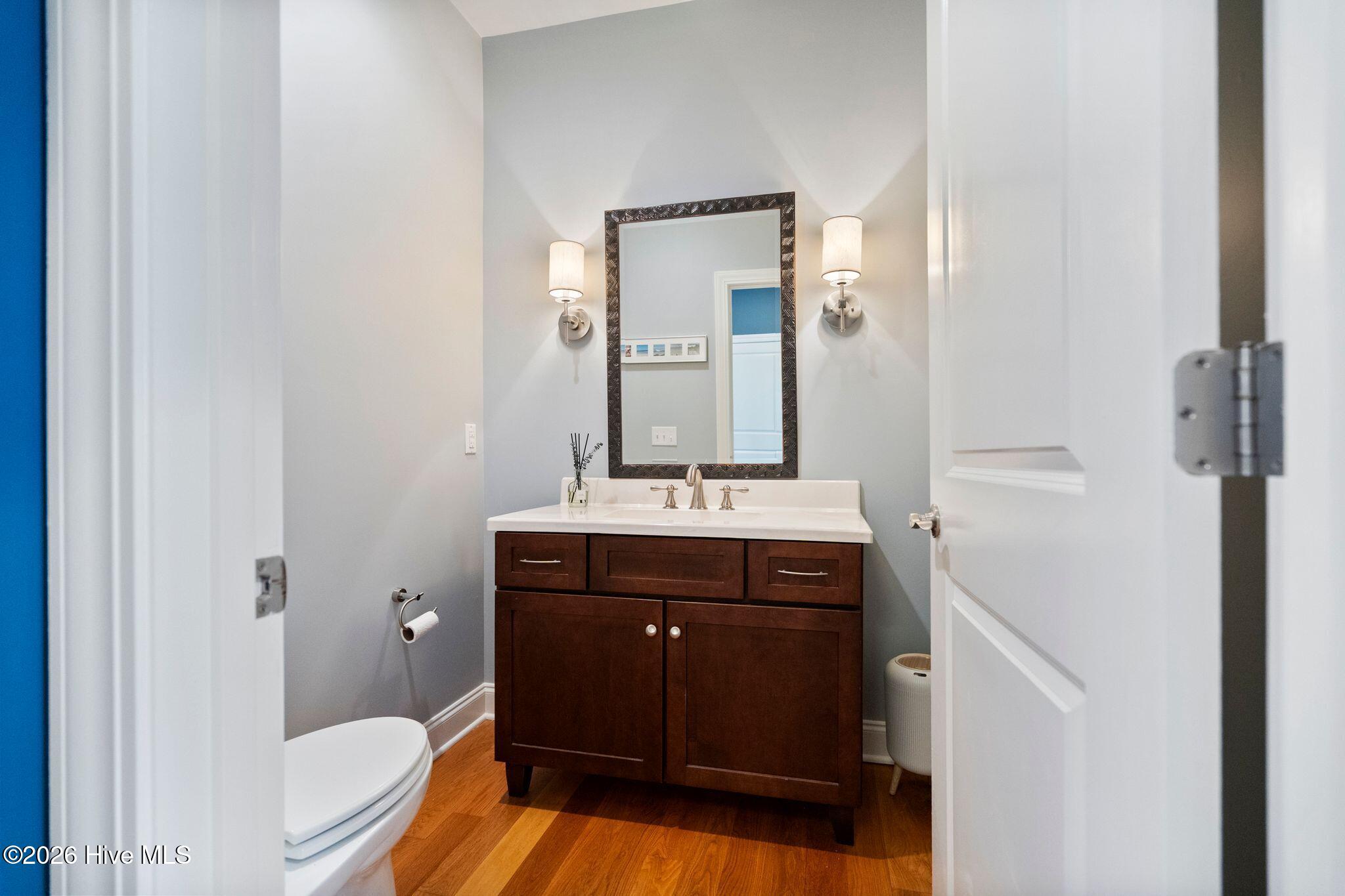 Bathroom with a dark wood vanity, framed mirror, and warm-toned wood flooring.