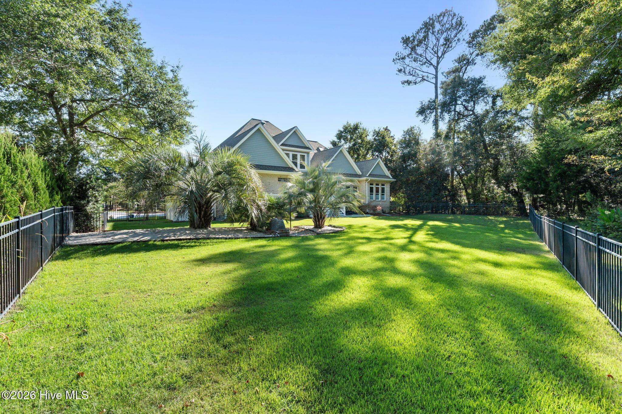 House behind a fenced lawn with palm trees and a paved patio.
