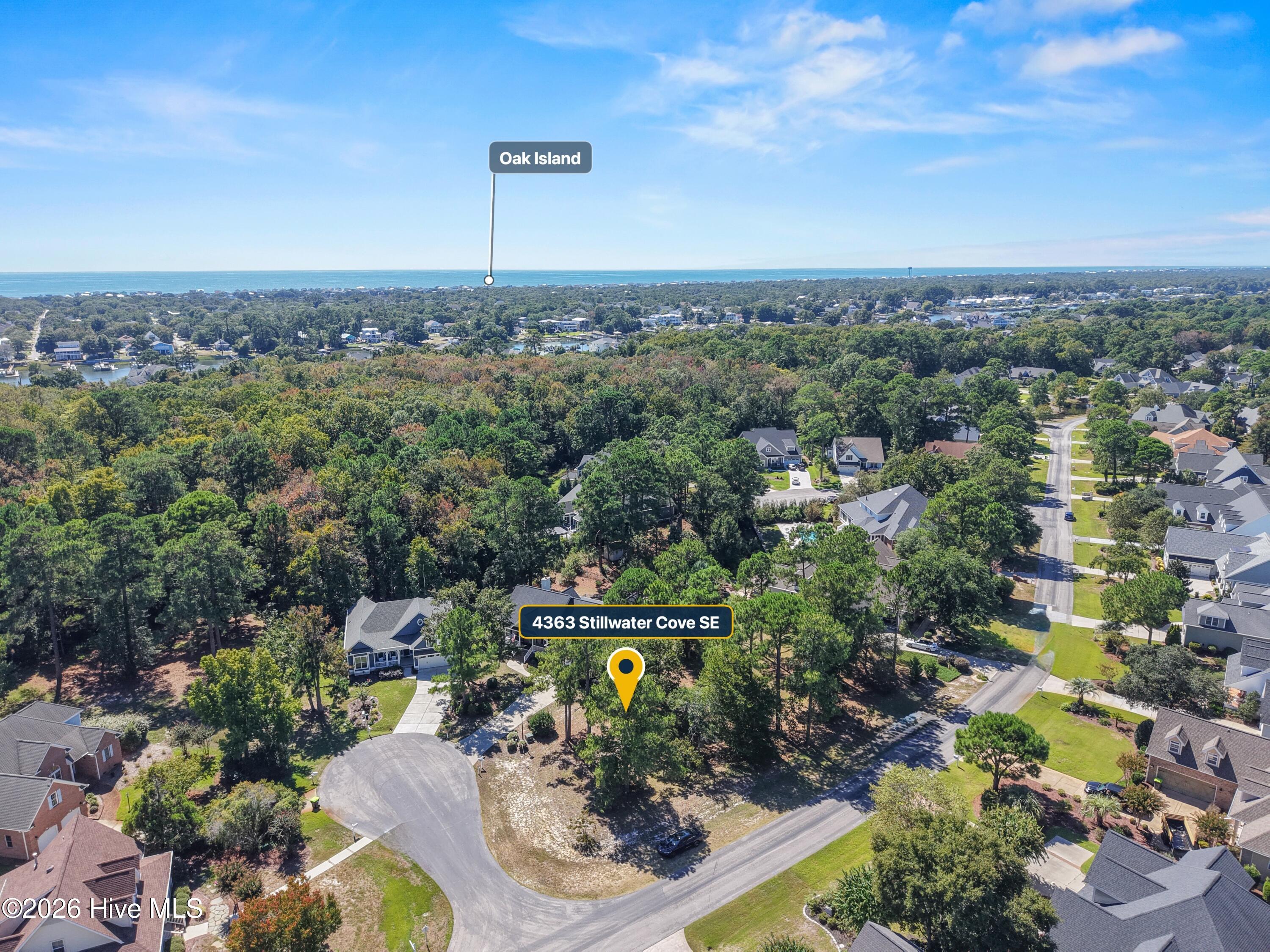 Aerial view of the marked home in a wooded neighborhood, with the ocean visible beyond it.