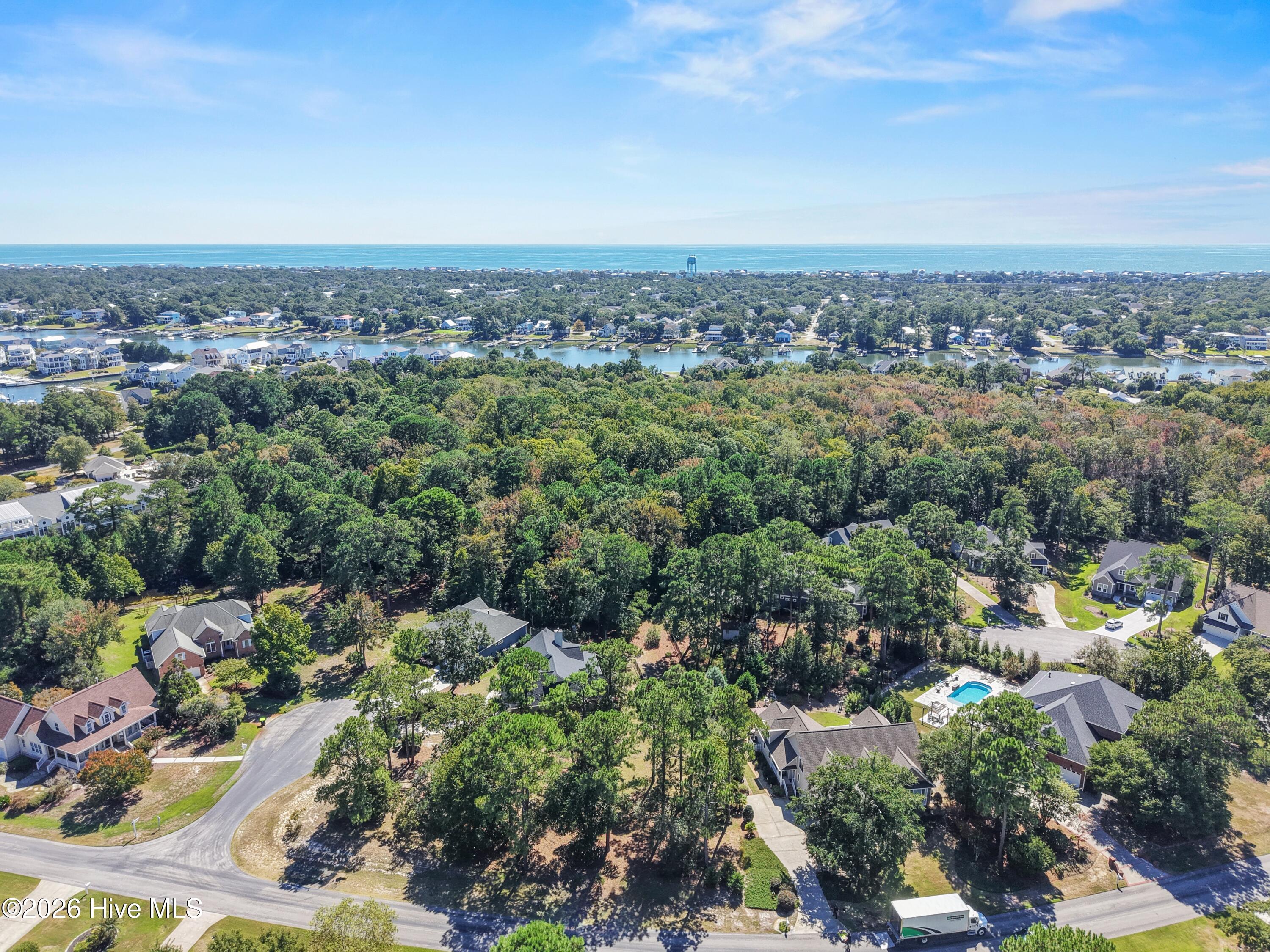 Aerial view of a wooded neighborhood, waterways, and homes with the ocean on the horizon.