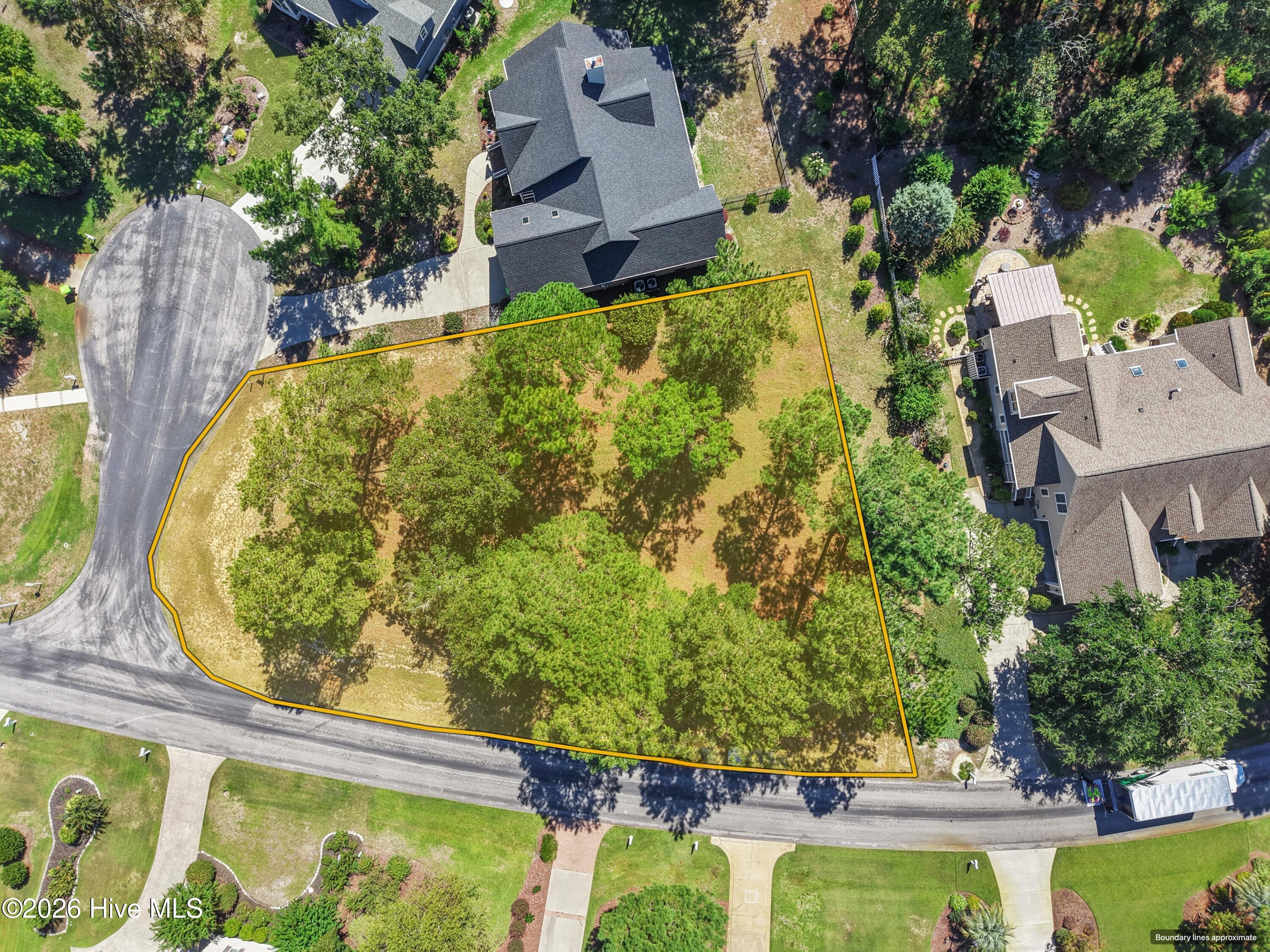 Aerial view of a vacant, tree-covered lot outlined in yellow between neighboring homes and streets.