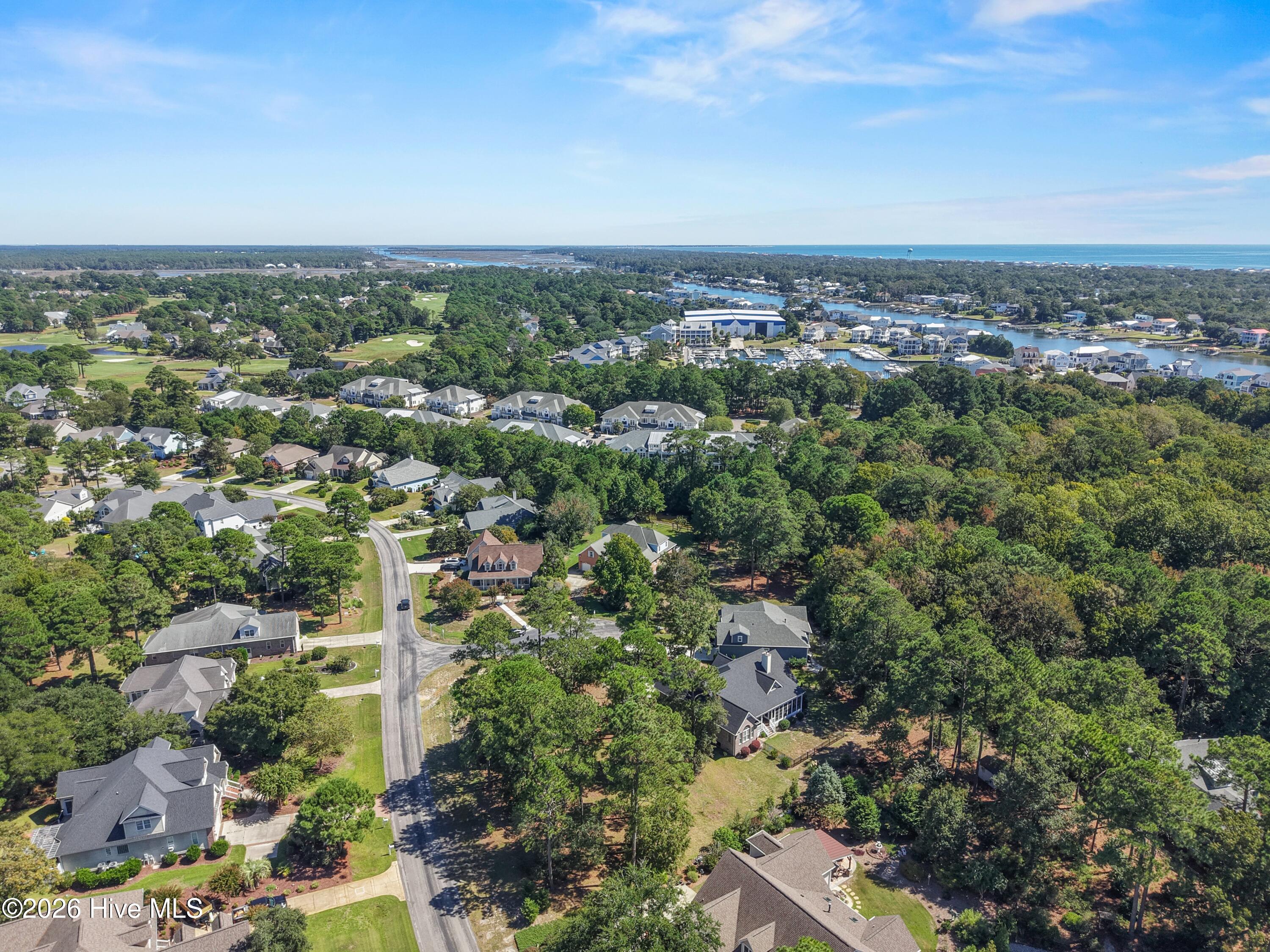 Aerial view of a coastal neighborhood with a golf course, marina, and ocean in the distance.