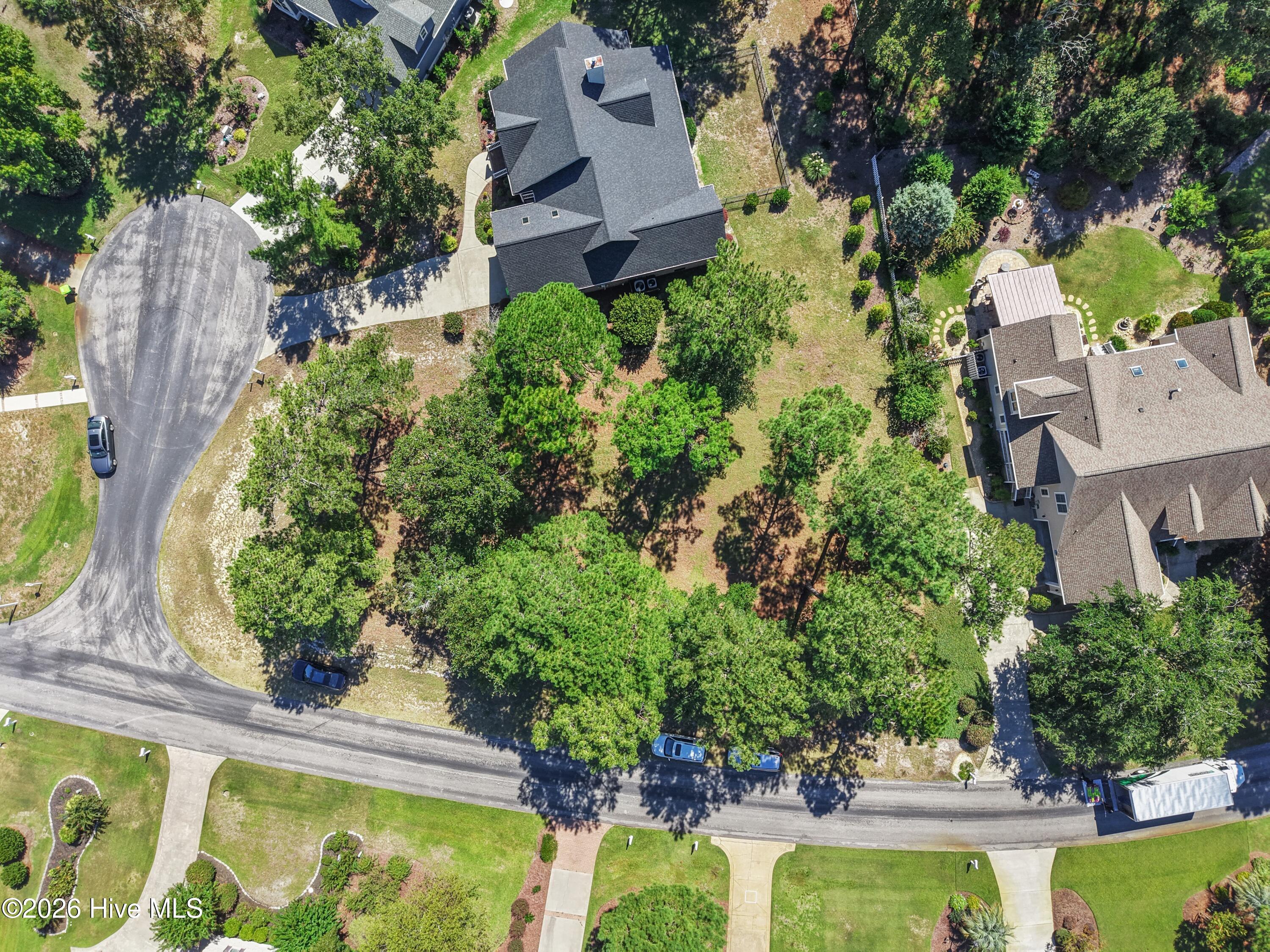 Aerial view of a house on a wooded lot beside a curving residential street.