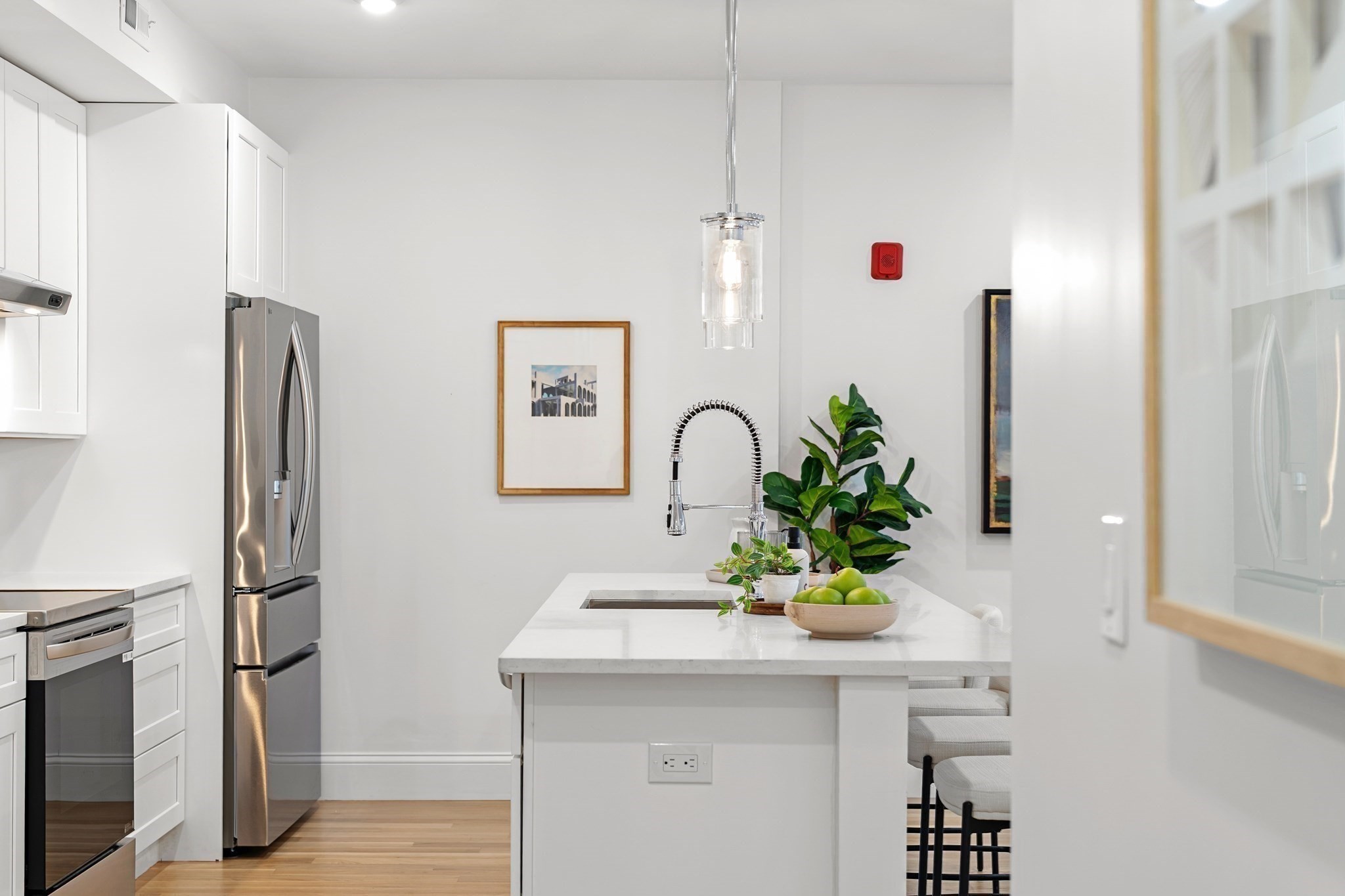 Modern white kitchen with a large island, spring-coil faucet, stainless appliances, and upholstered stools.
