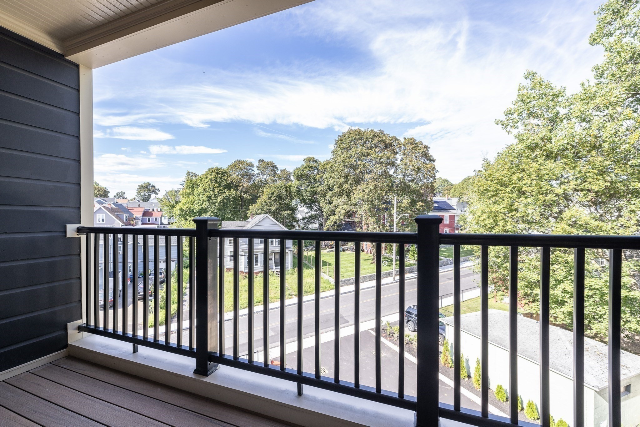 Covered apartment balcony overlooking a residential street and leafy trees.