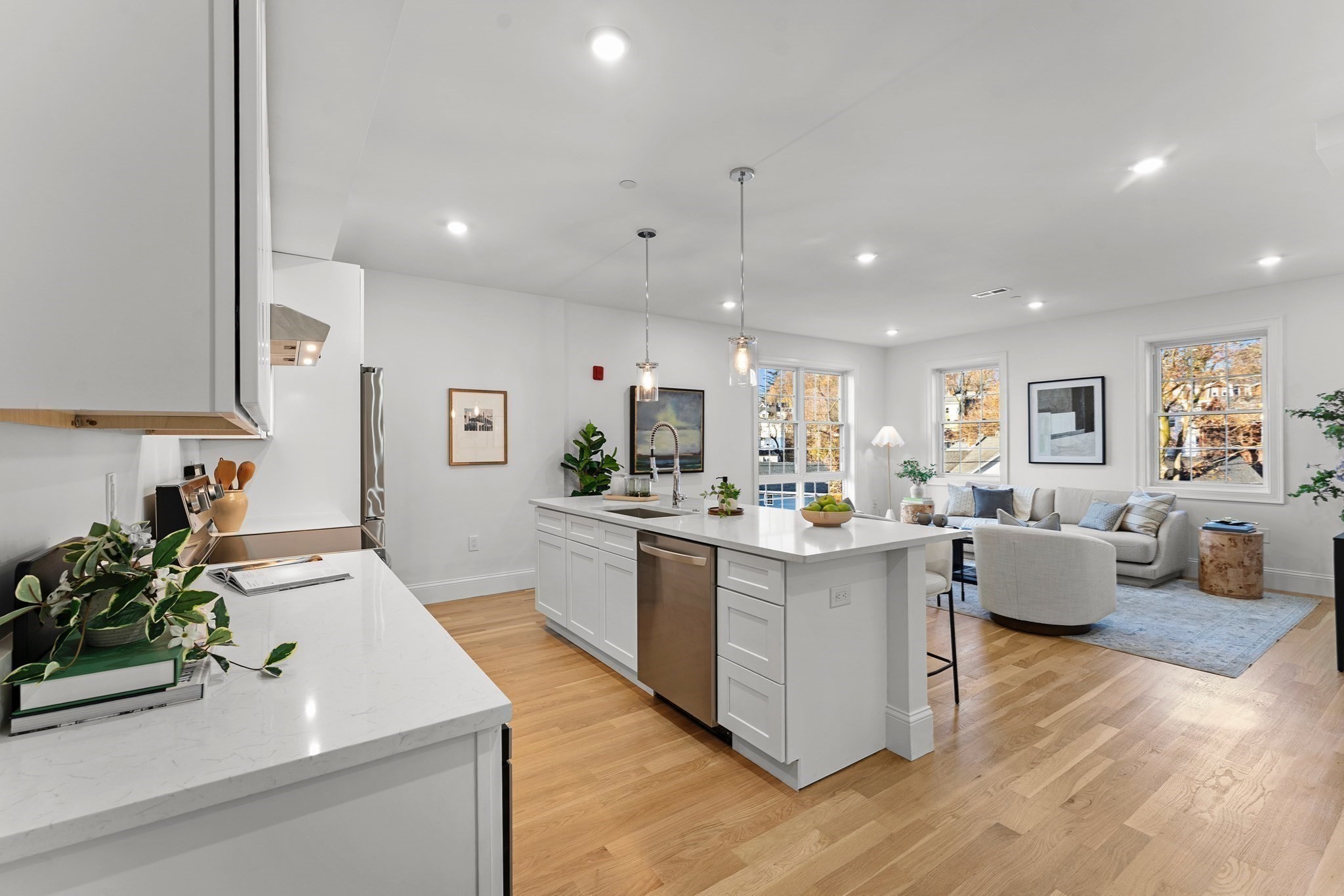 Open-plan kitchen and living area with a large white island, quartz counters, and hardwood floors.