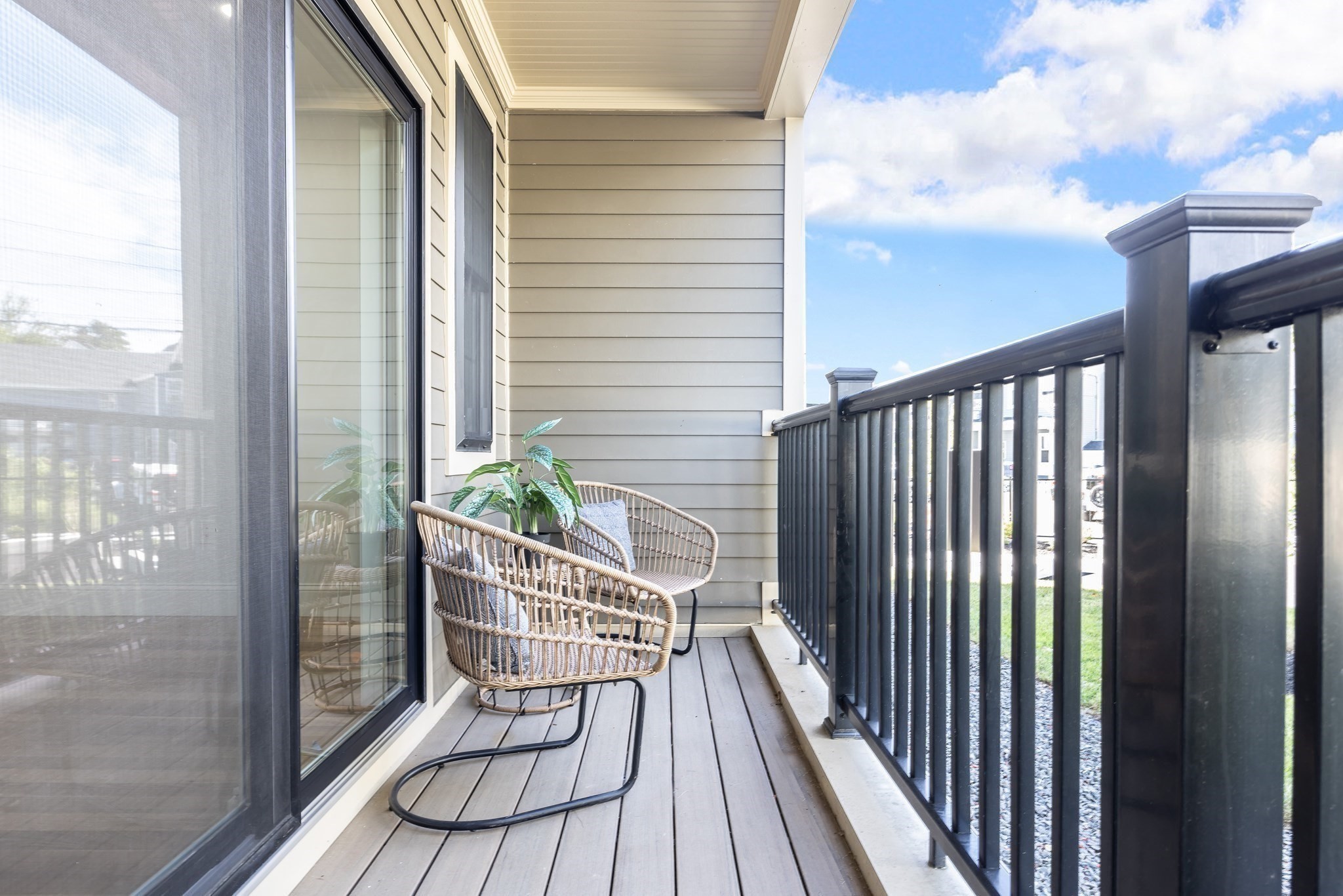 Furnished apartment balcony with woven chairs, a potted plant, and black metal railings.