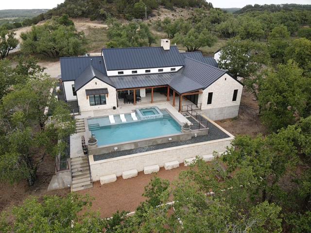 Aerial view of a stone house with a dark metal roof and pool on a wooded hillside.